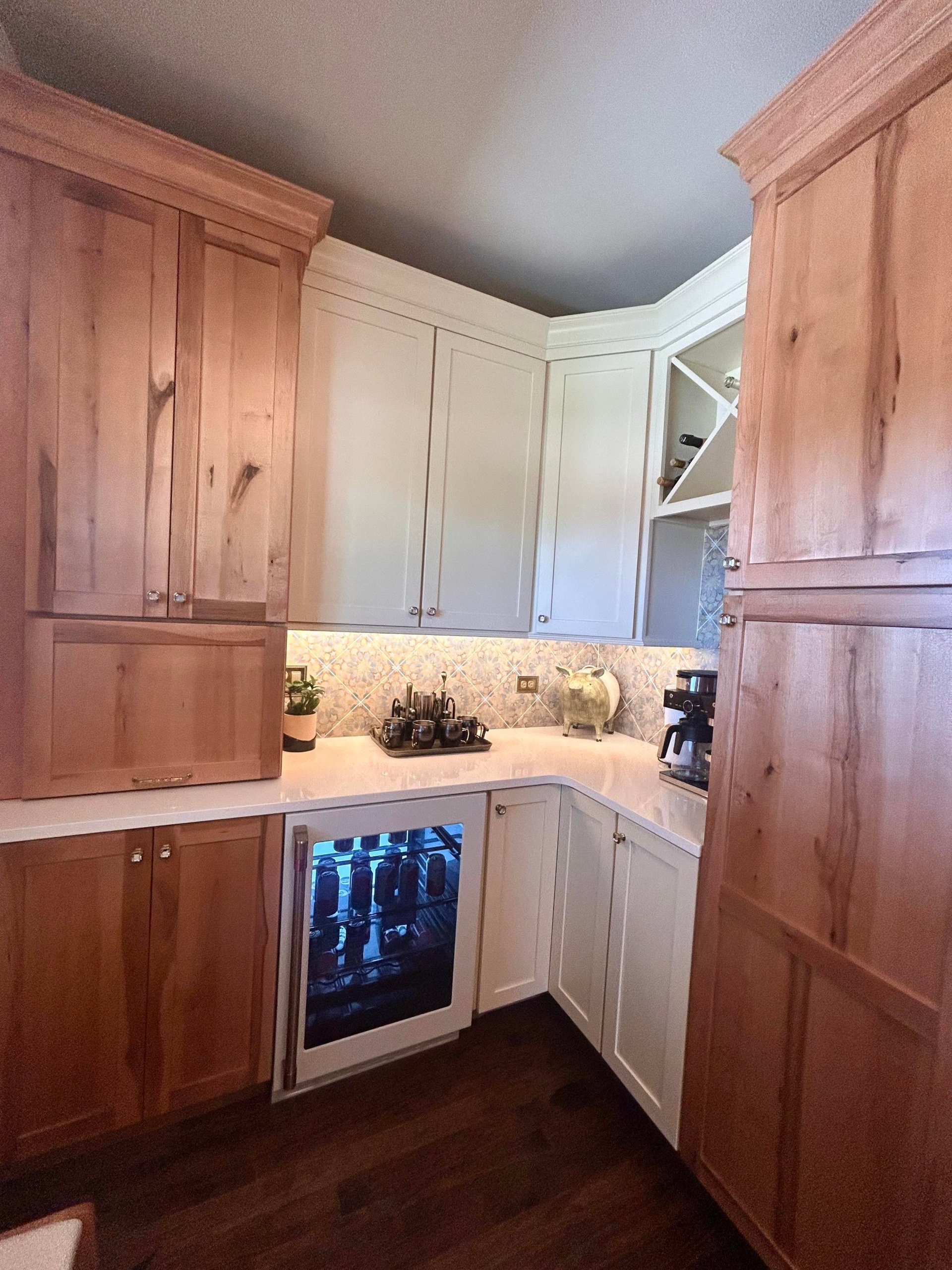 Small butler's pantry behind the Victorian kitchen with warm wood cabinets, cream uppers, a glass-front beverage fridge, coffee maker, wine storage cubbies, and the same Moroccan backsplash tile.