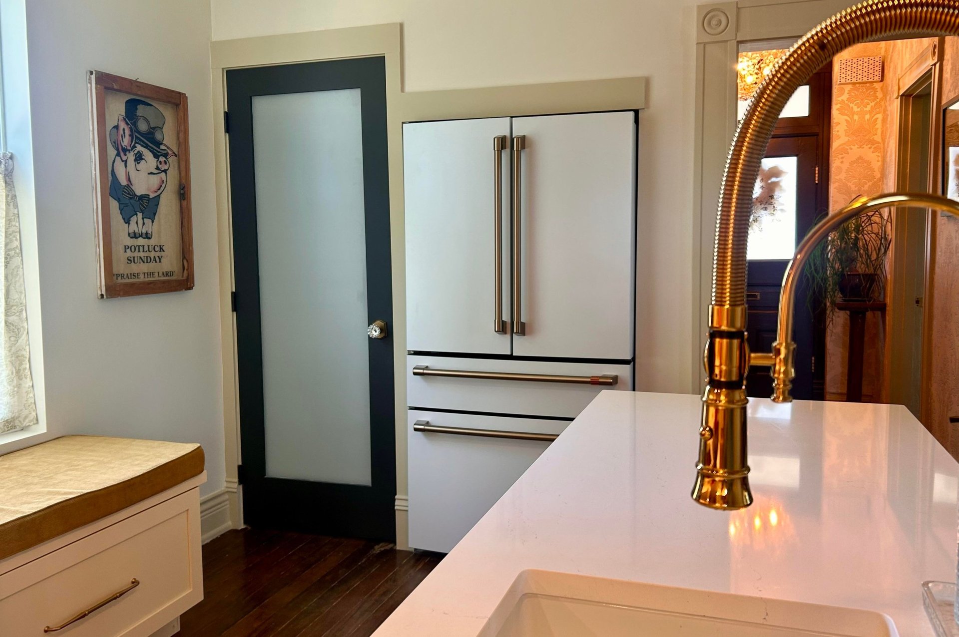 Matte white French-door GE Cafe refrigerator built into a shallow closet in the Victorian kitchen, with brushed bronze handles, a frosted glass pantry door beside it, and a vintage Potluck Sunday pig poster on the wall.