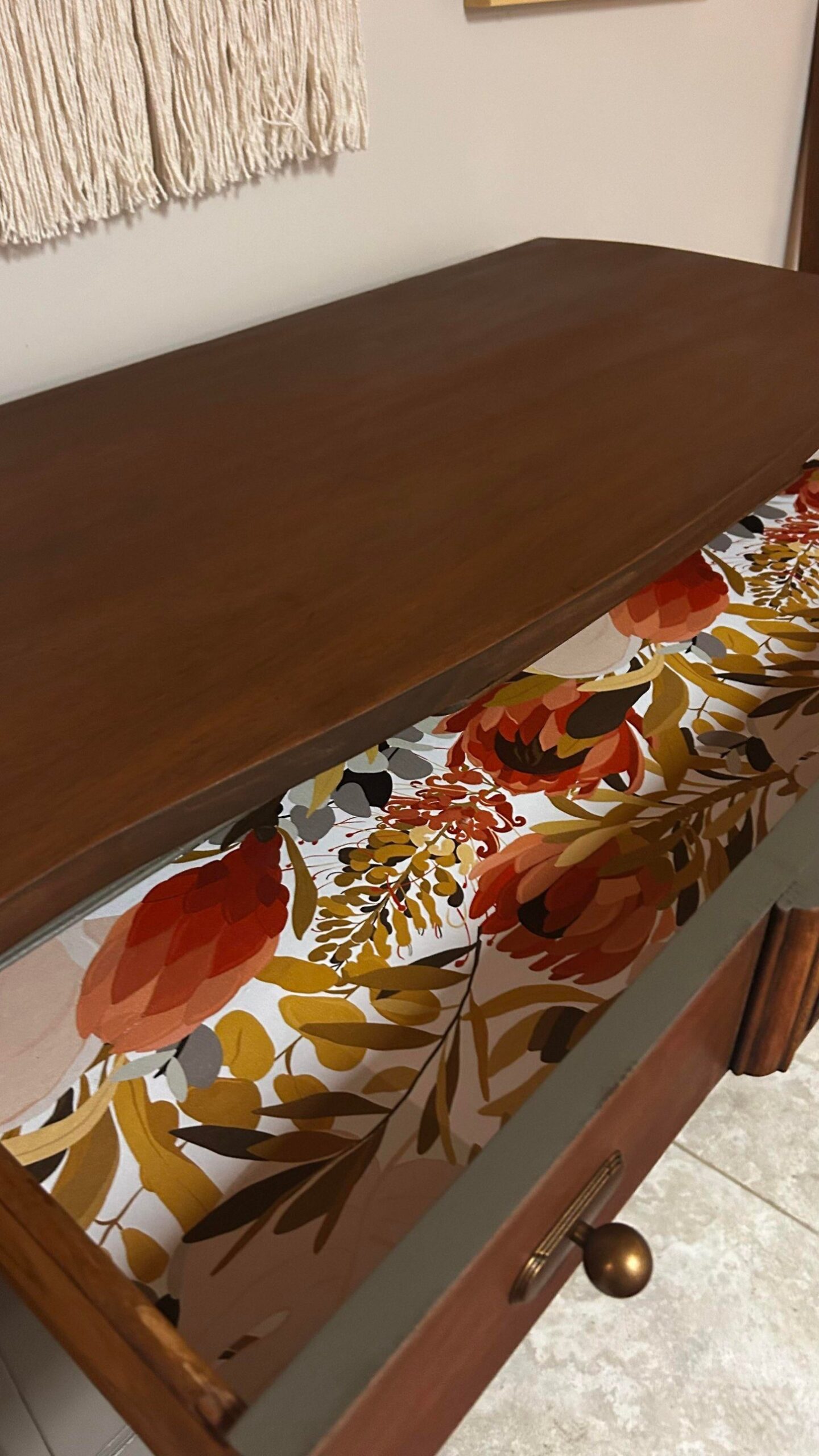 Close-up of a drawer interior lined with a bold floral print of red proteas, mustard foliage, and gray-green leaves on a cream background.