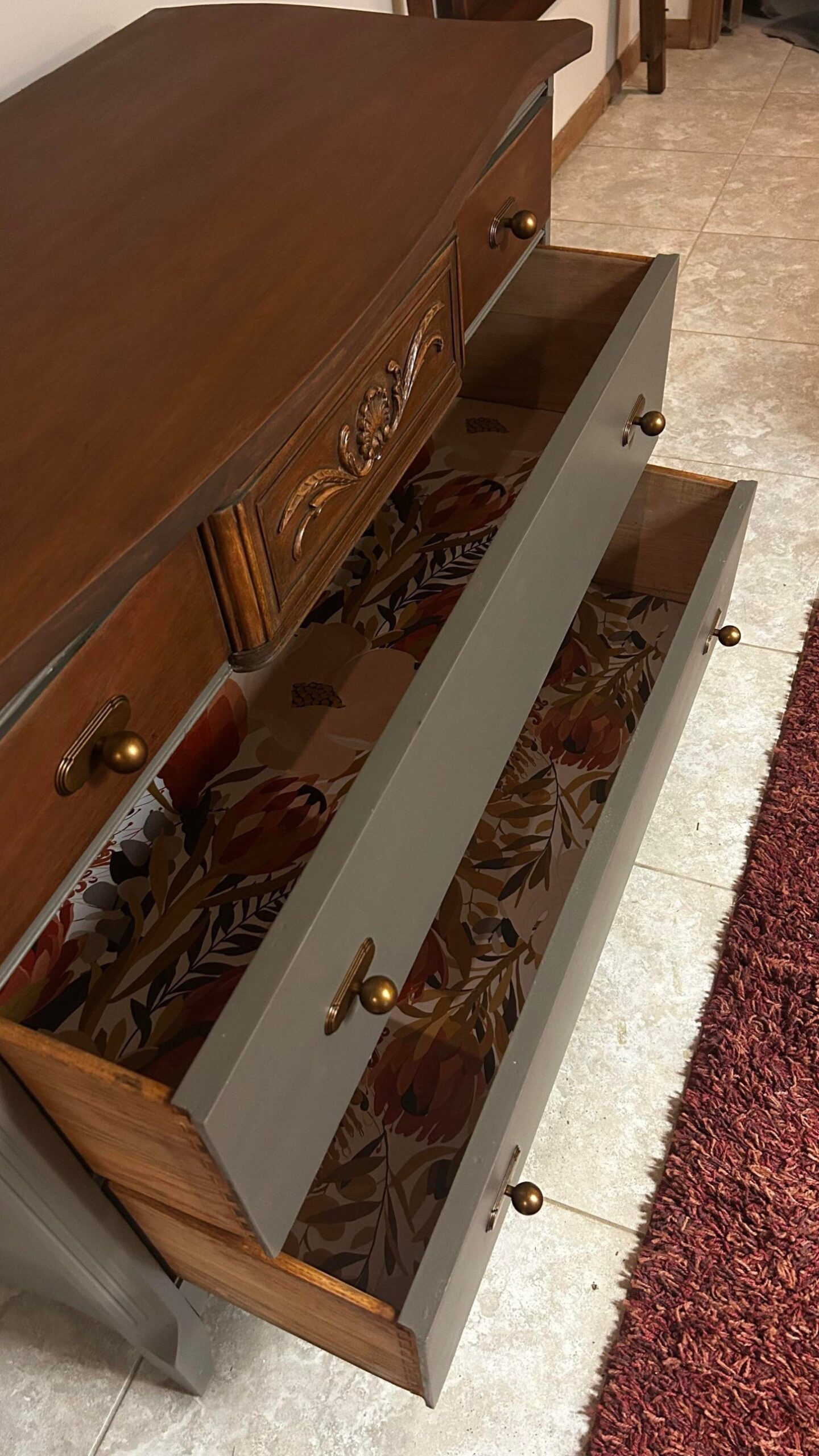 Two drawers of the walnut-and-olive dresser pulled open to reveal bright protea floral paper liners in rust red, mustard, dusty rose, and olive green.