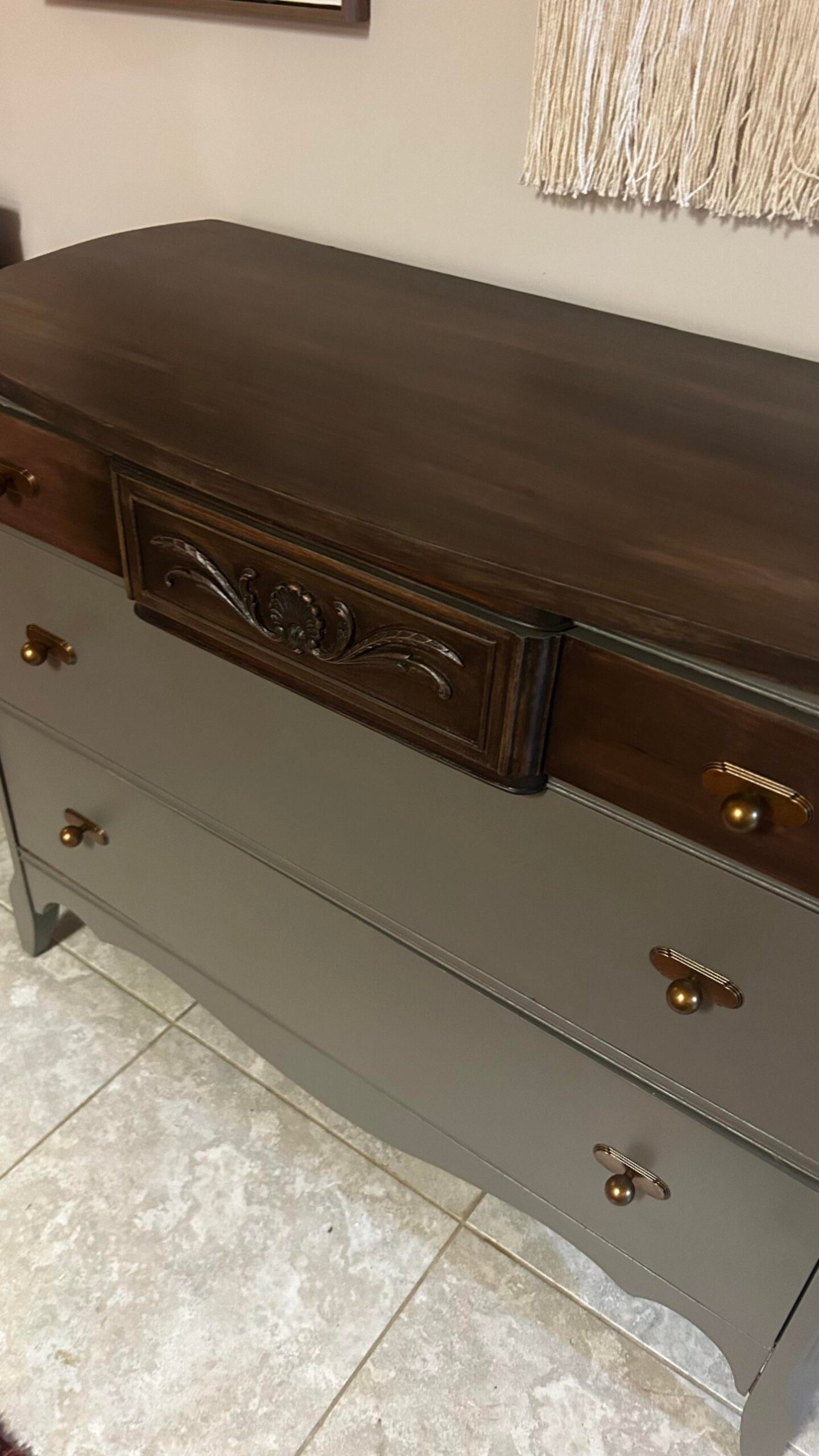 Close-up angled view of the dresser top finished in dark Kona stain, showing a near-black finish next to the carved center drawer and the olive-gray painted body.
