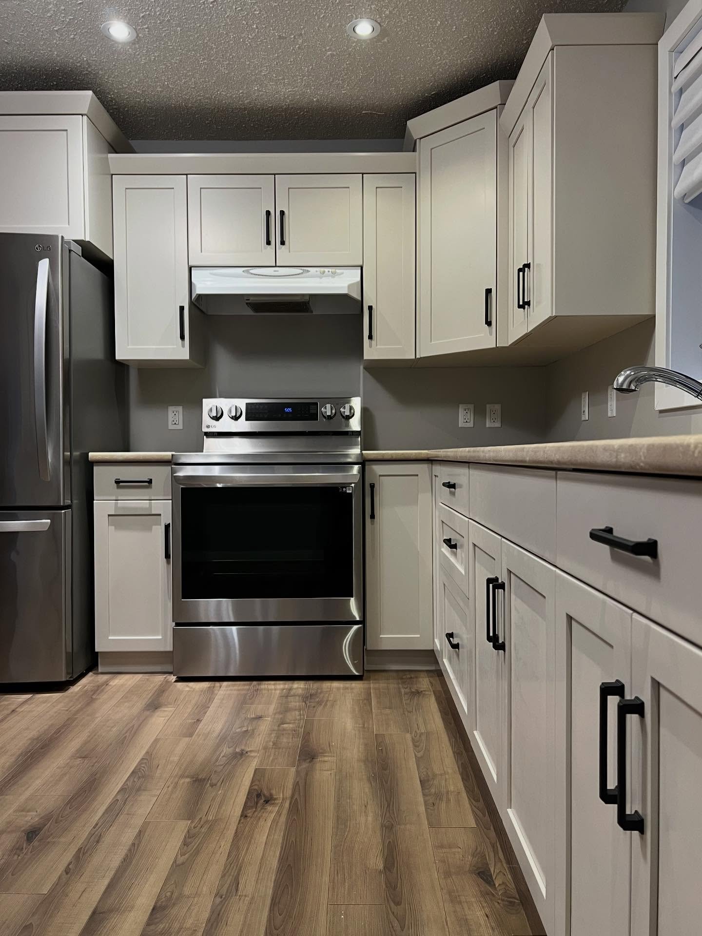 Kitchen in Sherwin-Williams Accessible Beige shot from the fridge side, with stainless LG fridge, electric range, white range hood, tan laminate counters wrapping to a chrome faucet on the right, and matte black bar pulls.