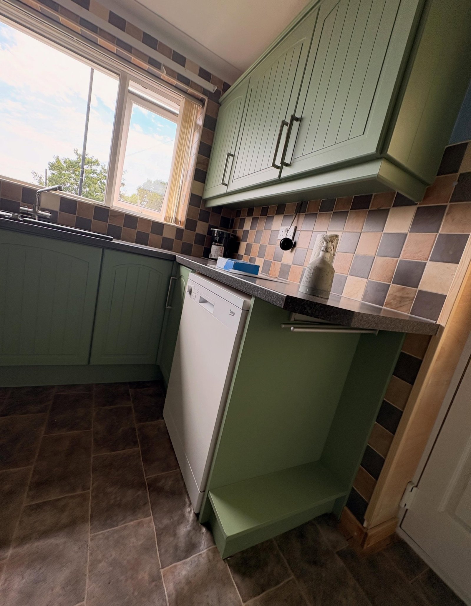 Close view of arched top cabinet doors painted in sage Farrow & Ball Breakfast Room Green matte finish, with checkerboard tile below.