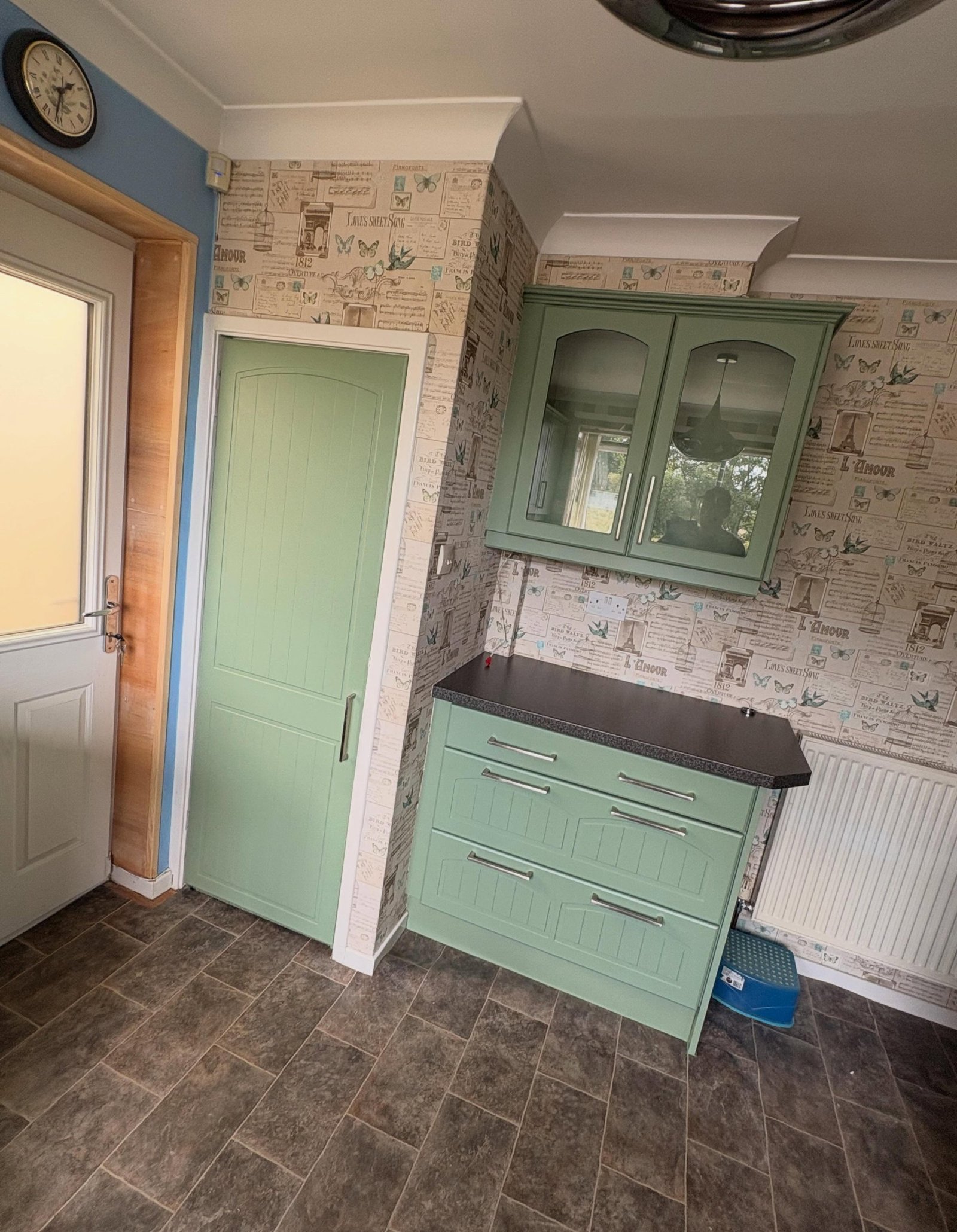 Sage green painted cabinet door and arched glass-front cabinet, tilted view, daylight hitting the matte finish.