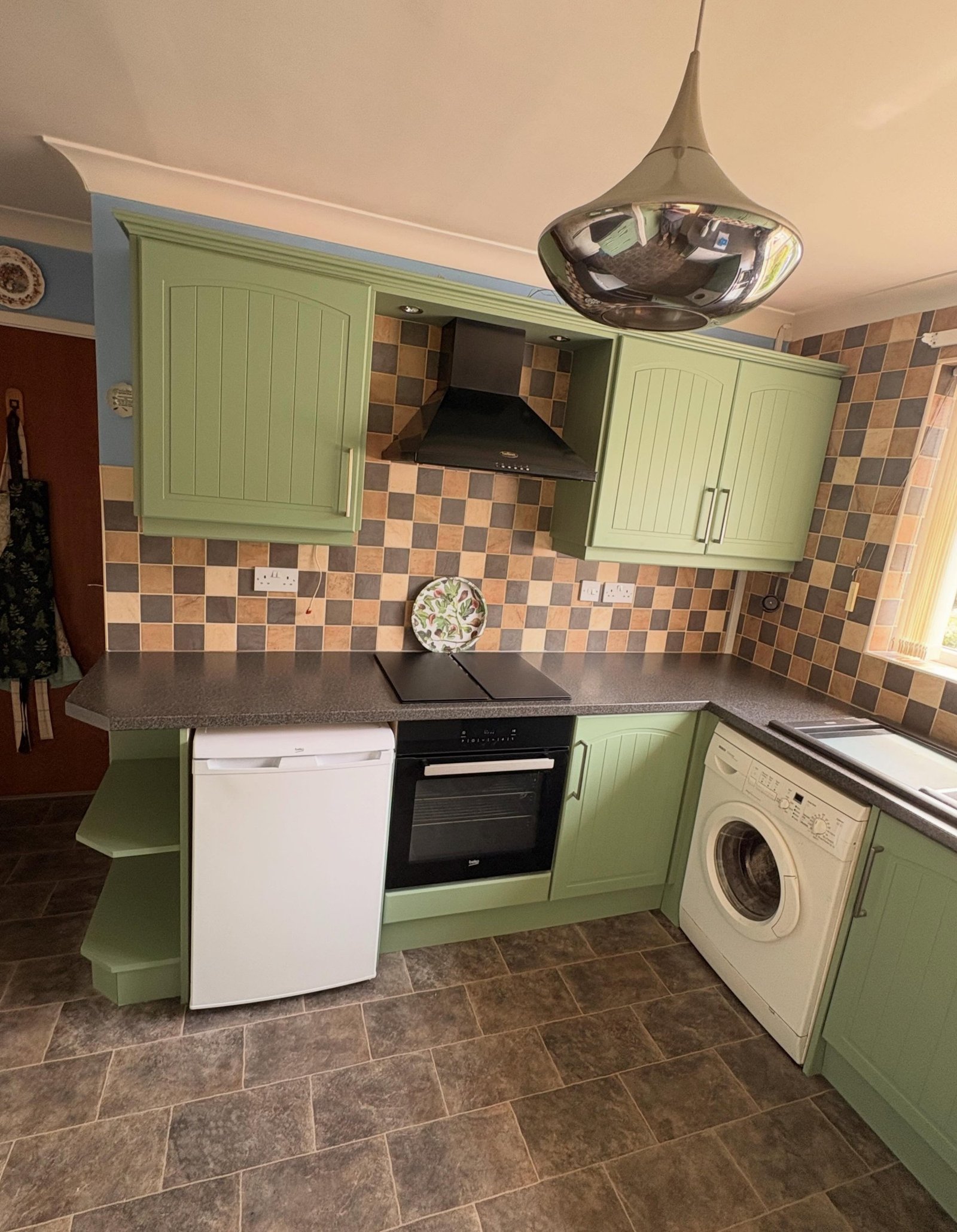 Painted sage green pantry door, drawers and glass-front wall cabinet in Farrow & Ball Breakfast Room Green against vintage wallpaper.