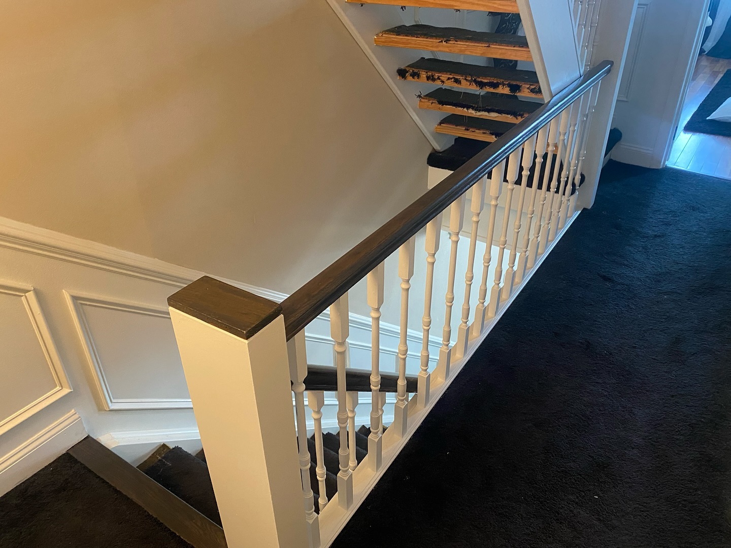 In-progress stair showing bare wood treads after the dark carpet was pulled, with white spindles and a dark stained handrail already finished.