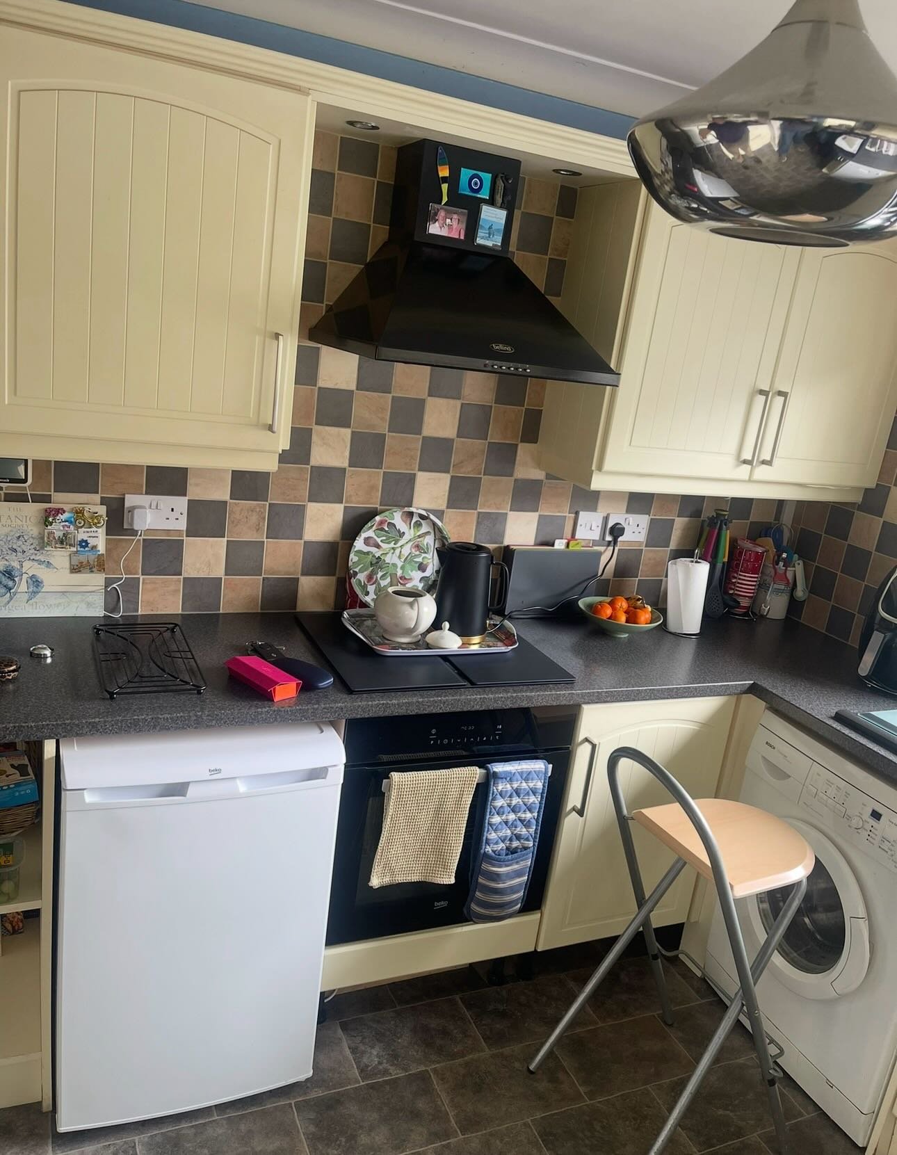 U-shaped kitchen with cream arched cabinets, patchy beige and grey checkerboard tile backsplash, black cooker hood, and freestanding white appliances, before painting.
