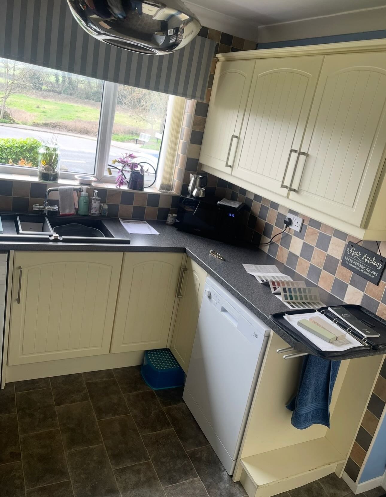 Close view of cream cabinets flanking a black cooker hood, with brown, grey and cream patchwork tile backsplash behind the cooktop.