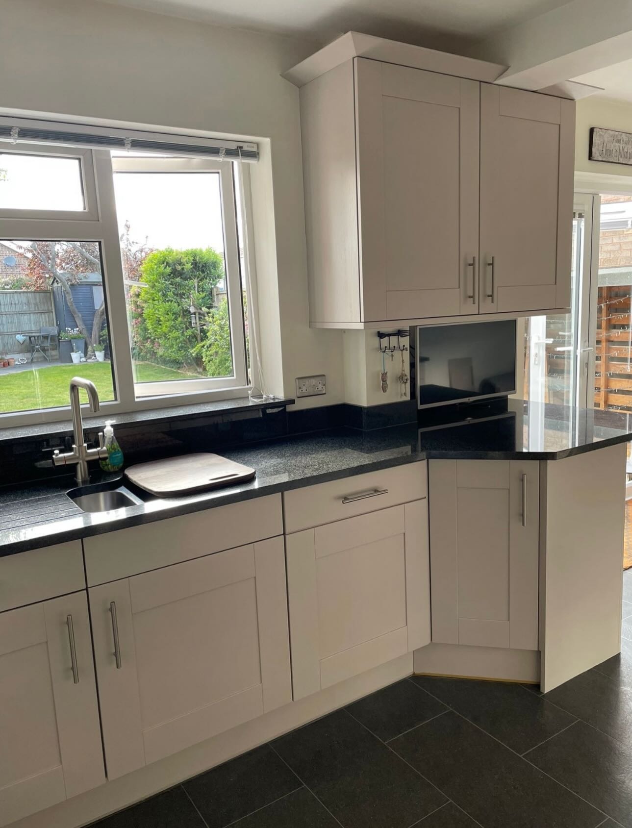 Angled view of the cashmere satin cabinets around the stainless chimney hood and oven, with black granite worktops and a sitting area visible to the left.