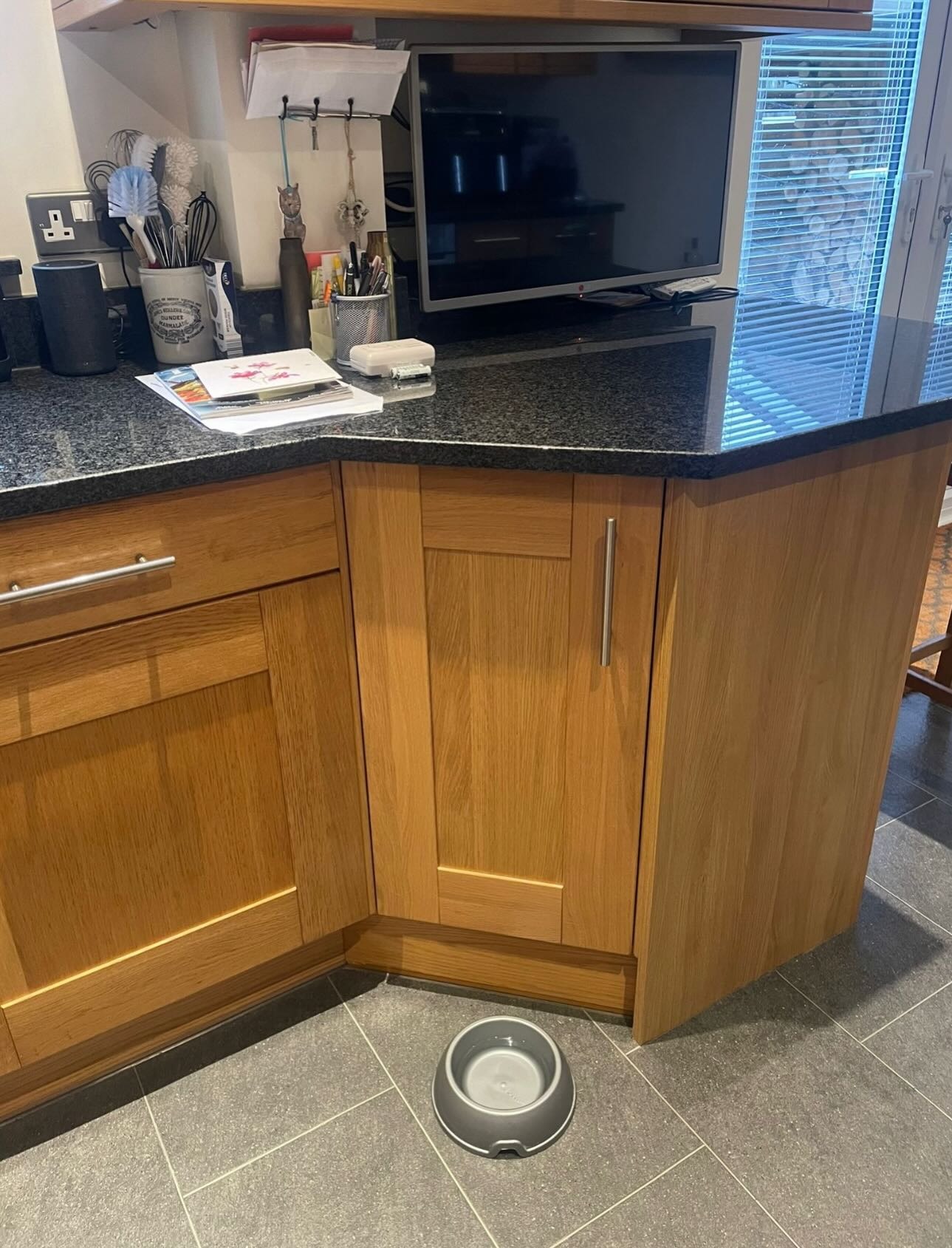 Wide view of the finished kitchen painted cashmere satin with a stainless chimney hood, built-in oven, induction hob, and dark granite worktops over gray tile flooring.