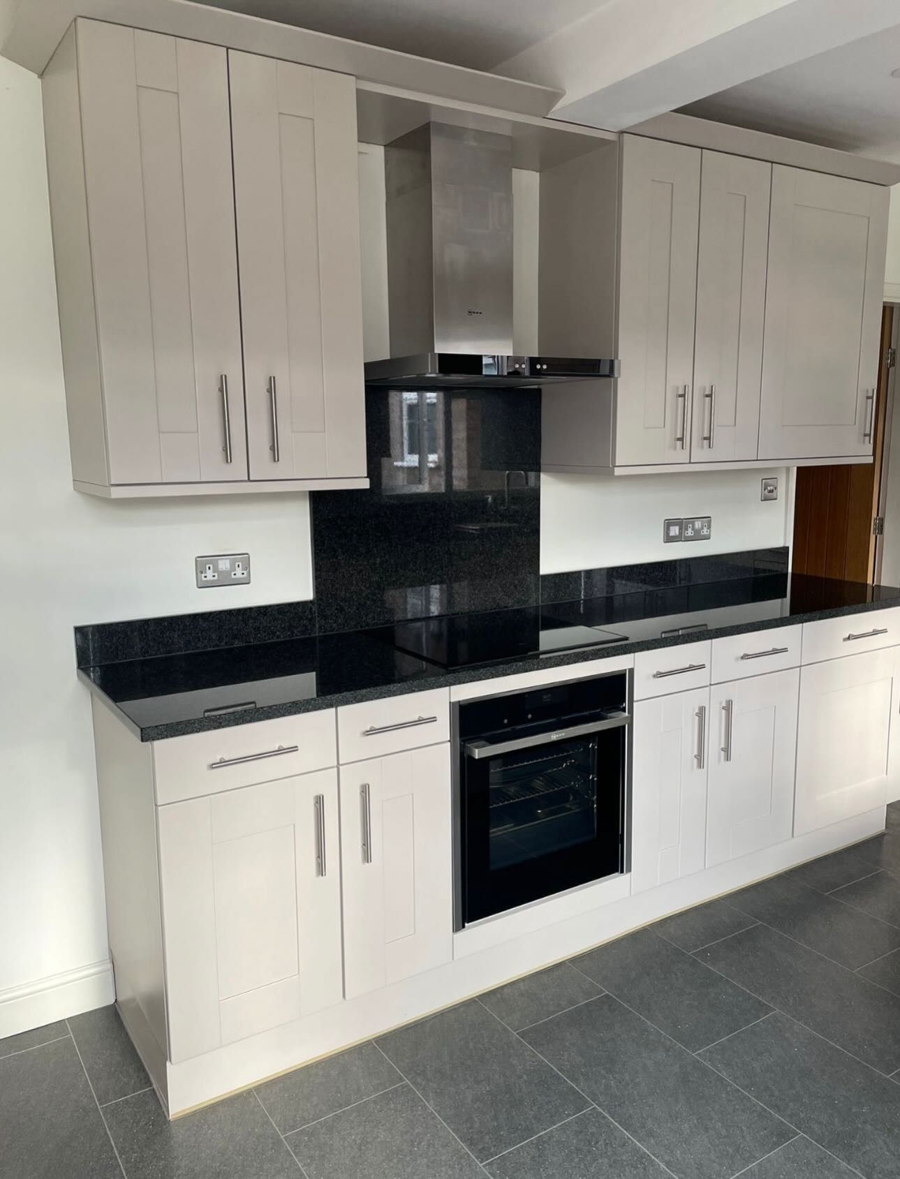 Cashmere satin cabinets around a stainless sink under a window looking out to a green garden, with a corner microwave shelf and open patio door.