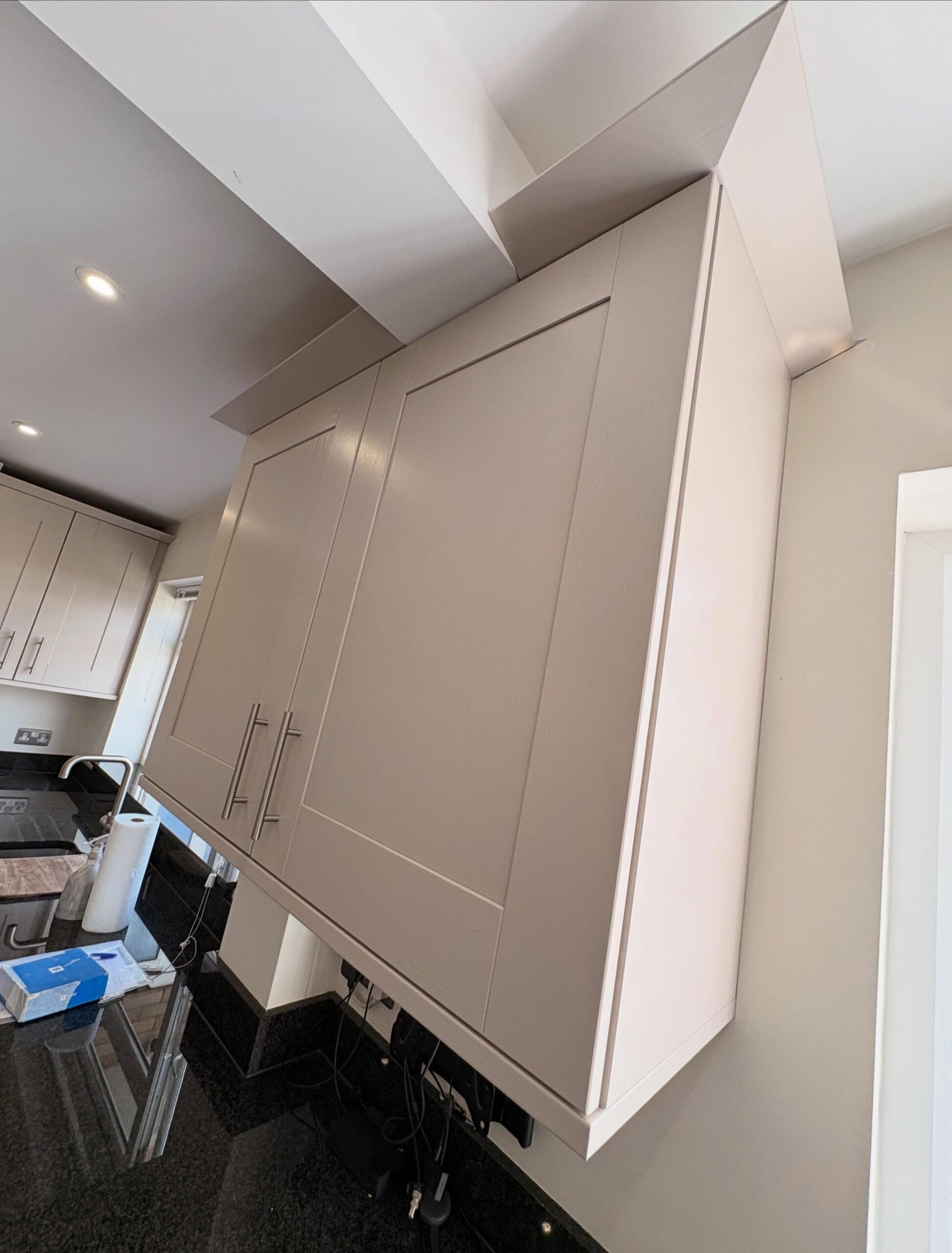 Close up of a pair of wall cabinets painted in cashmere satin, with the stainless bar handles and the subtle grain of the shaker frame visible.