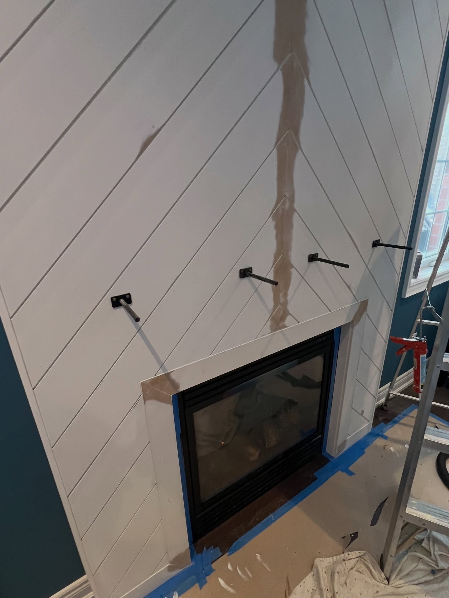 Close-up angled view of chevron panels after mudding and sanding the center seam, with mantel brackets installed and the firebox trimmed in white.