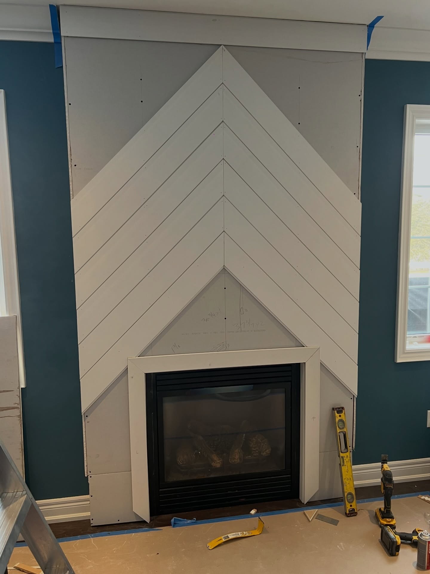 White chevron pattern made of mitered strips installed across the full wall with the center peak sitting just above the newly trimmed firebox opening.