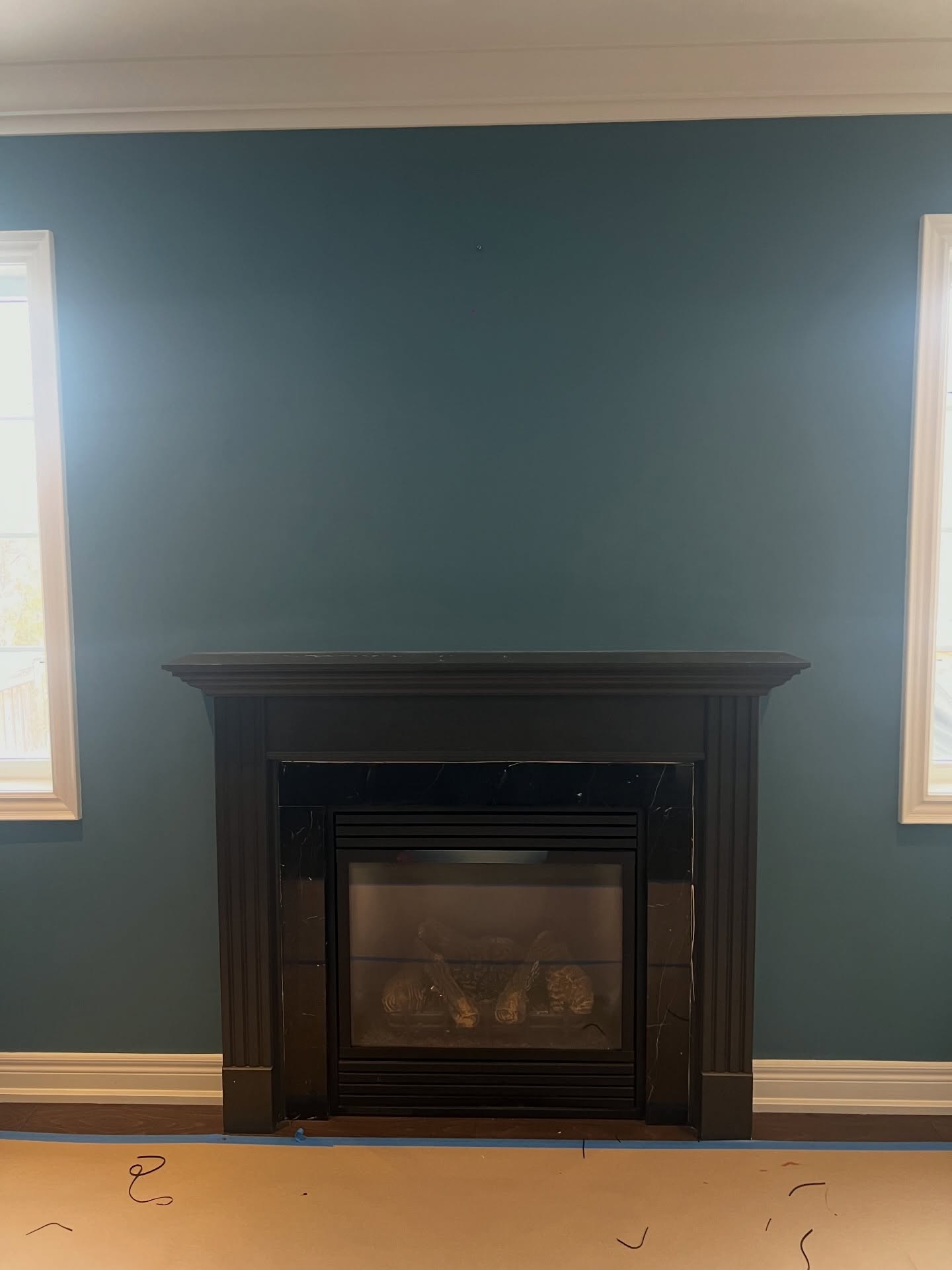 Straight-on view of the dark espresso mantel between two tall windows with a wide empty teal wall stretching above the mantel to the ceiling.