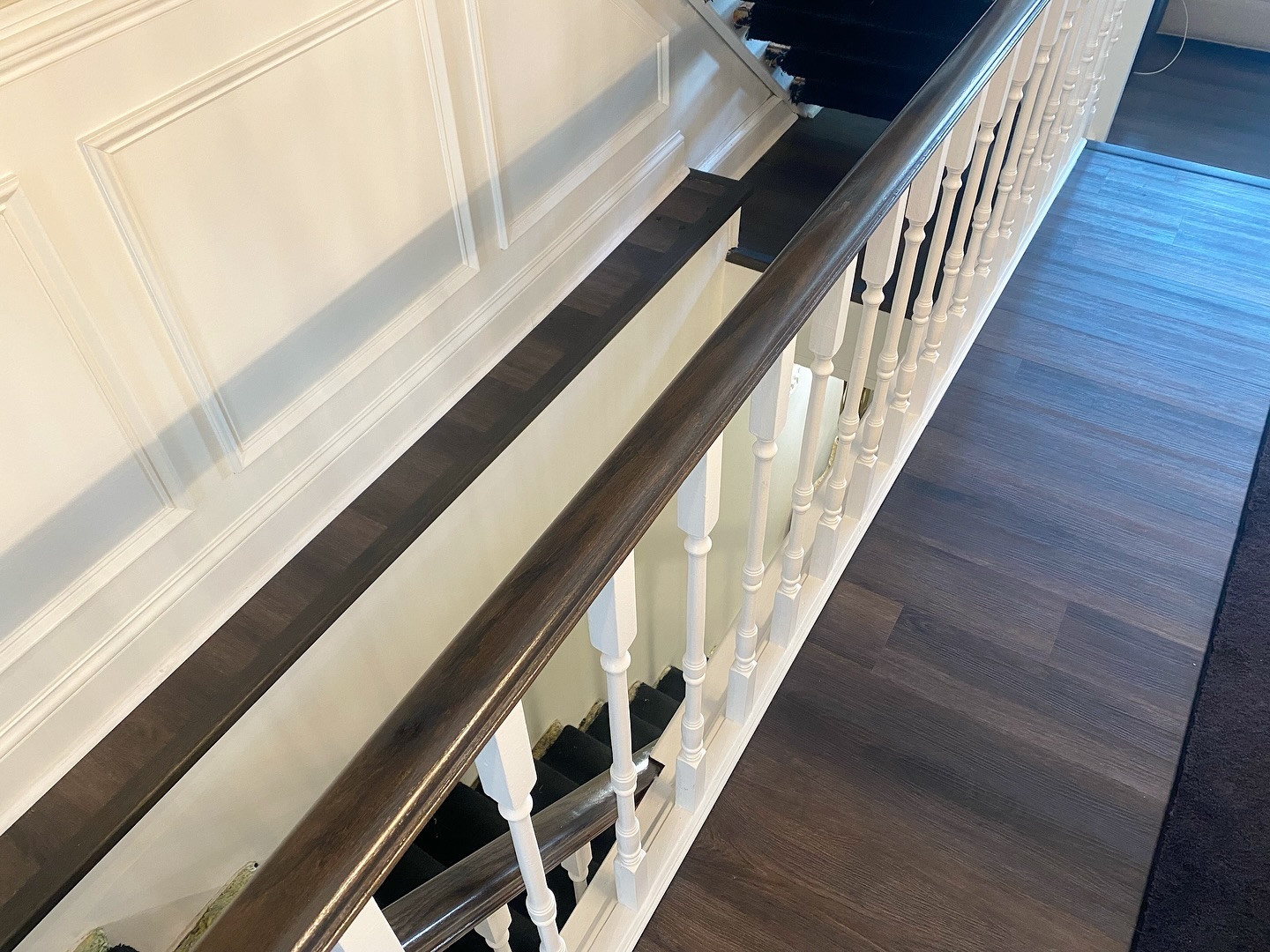 Angled view down the length of the custom dark stained handrail, with the matching tone dark wood floor visible to the right.