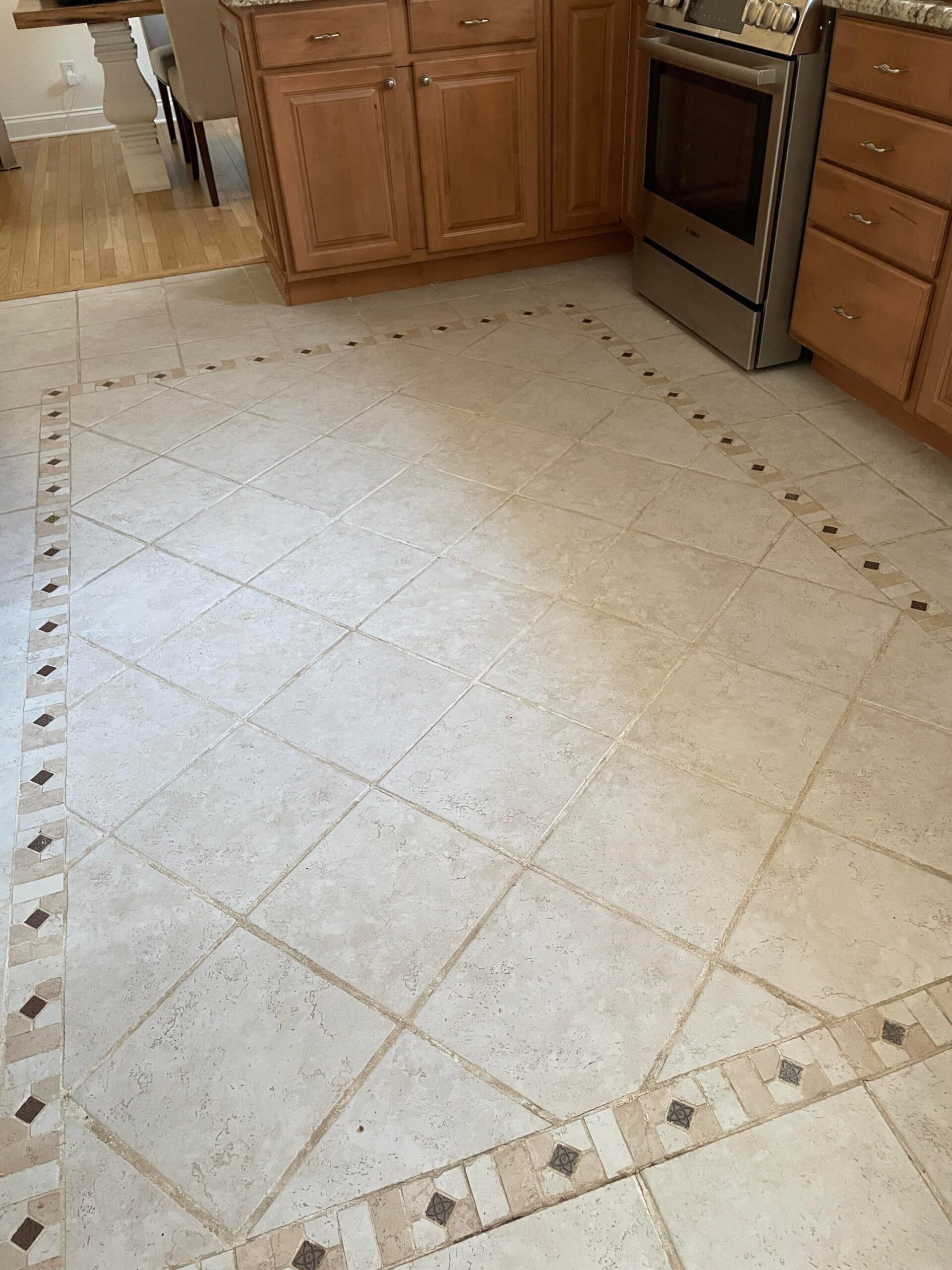 Travertine tile floor laid on the diagonal with inlaid dark diamond accents running along the perimeter in a kitchen with honey oak cabinets.