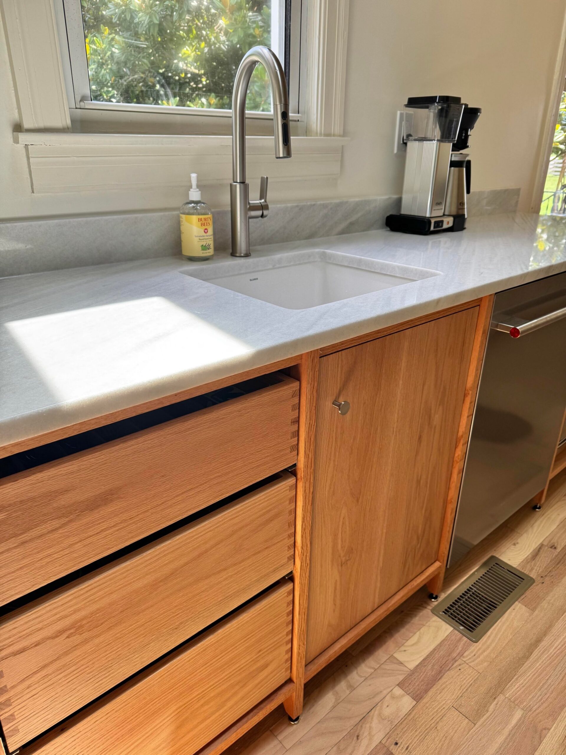Angled view of the finished kitchen showing the marble counter, undermount sink, hand soap, stainless faucet, and a Moccamaster coffee maker in the far corner.