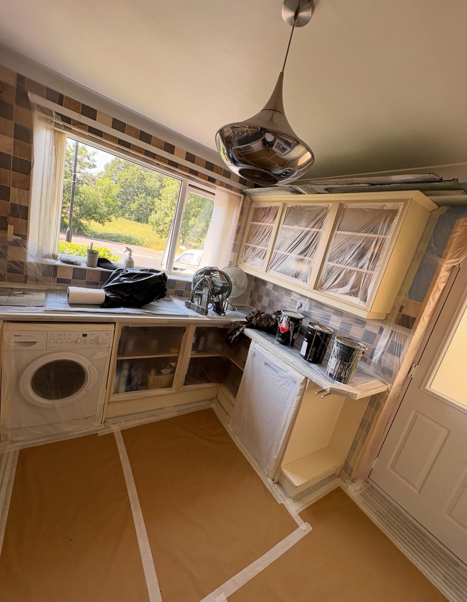 Kitchen cabinets, worktops, floor and walls covered in plastic sheeting and masking paper during prep for a spray paint job.