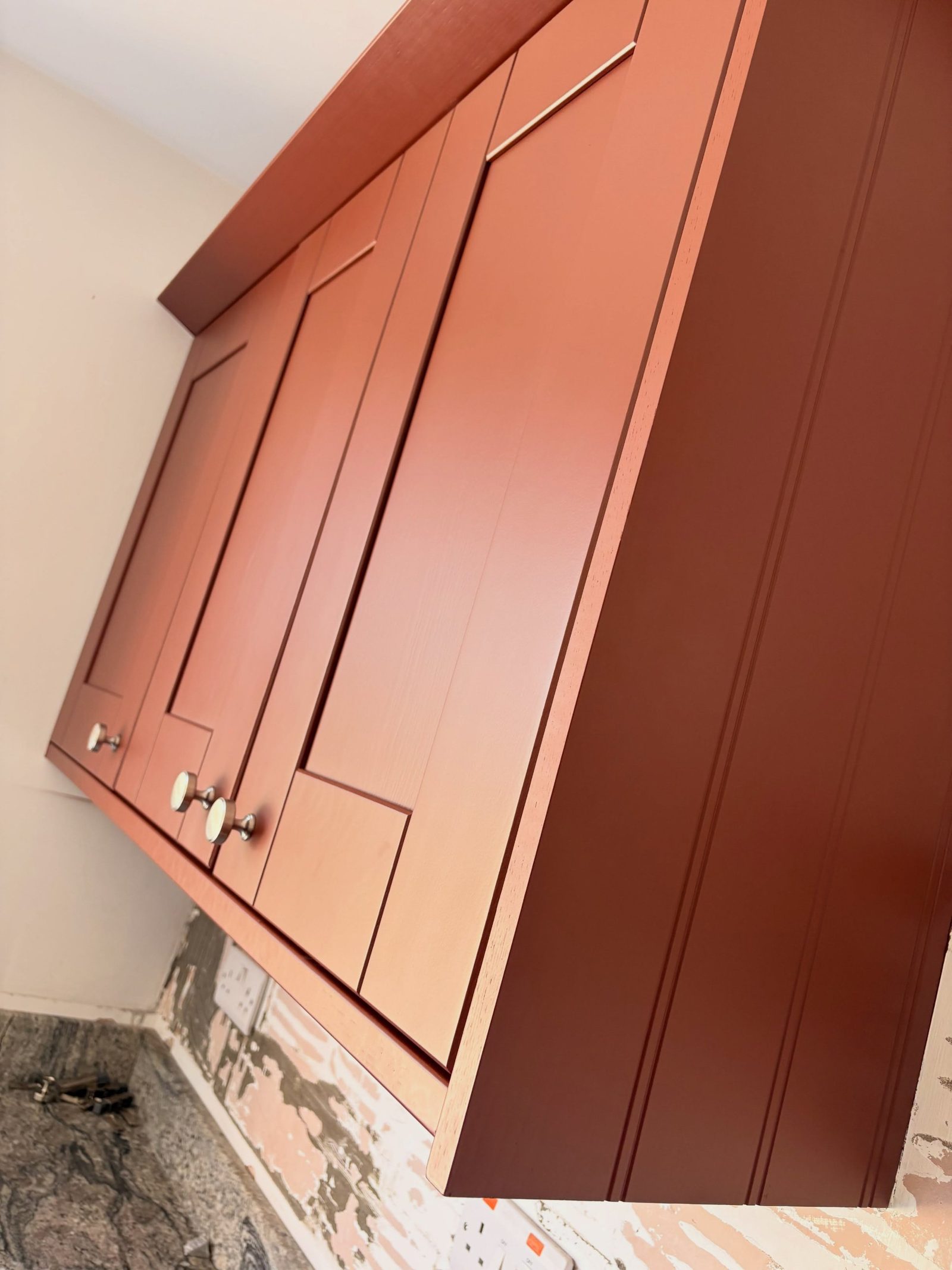 Close-up of chrome round knobs and cup-pulls on cabinet doors painted Farrow & Ball Etruscan Red matte.