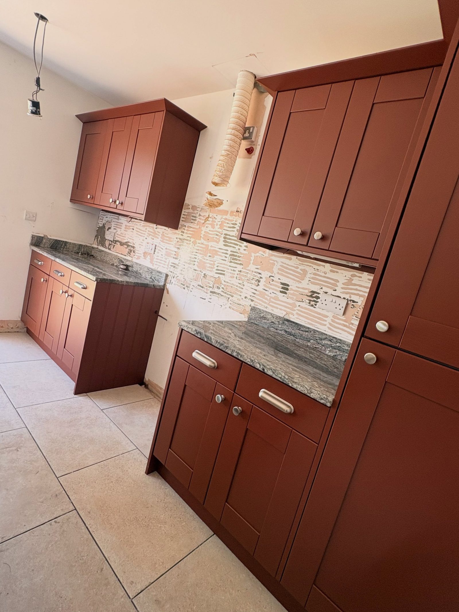 Finished kitchen with cabinets painted Farrow & Ball Etruscan Red, keeping the original green-gray granite island, chrome handles, and travertine floor.