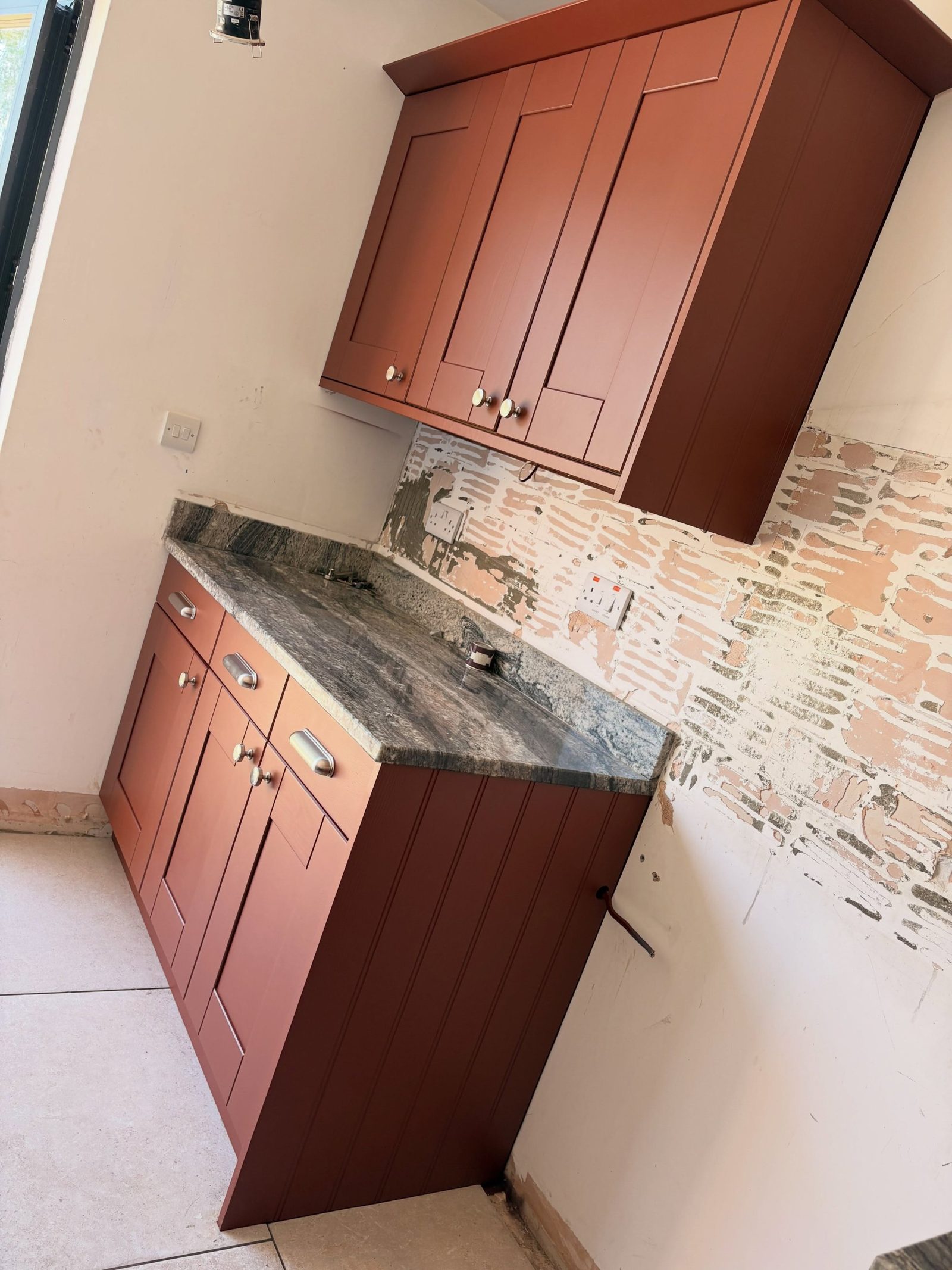 Floor-to-ceiling pantry units painted Etruscan Red in the corner of the finished kitchen, with chrome knobs and column radiator.