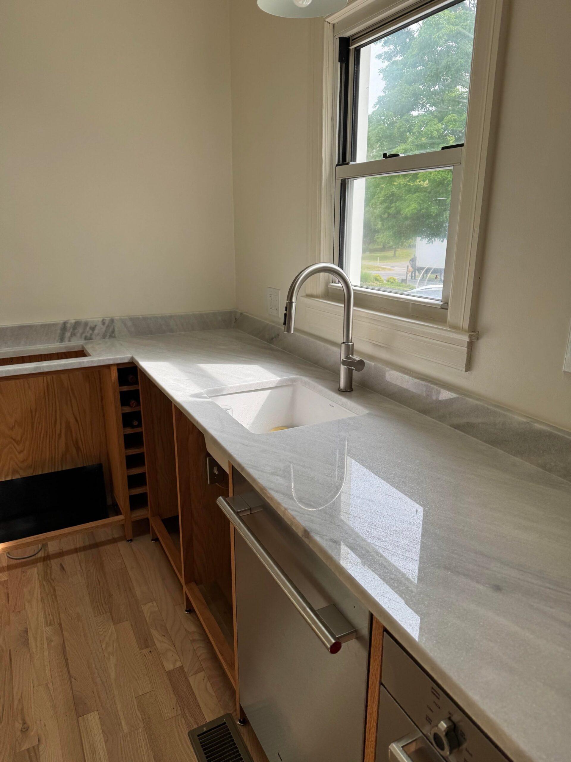 Wide shot of the completed white marble counter and undermount sink with the oak frames below still empty of drawers.