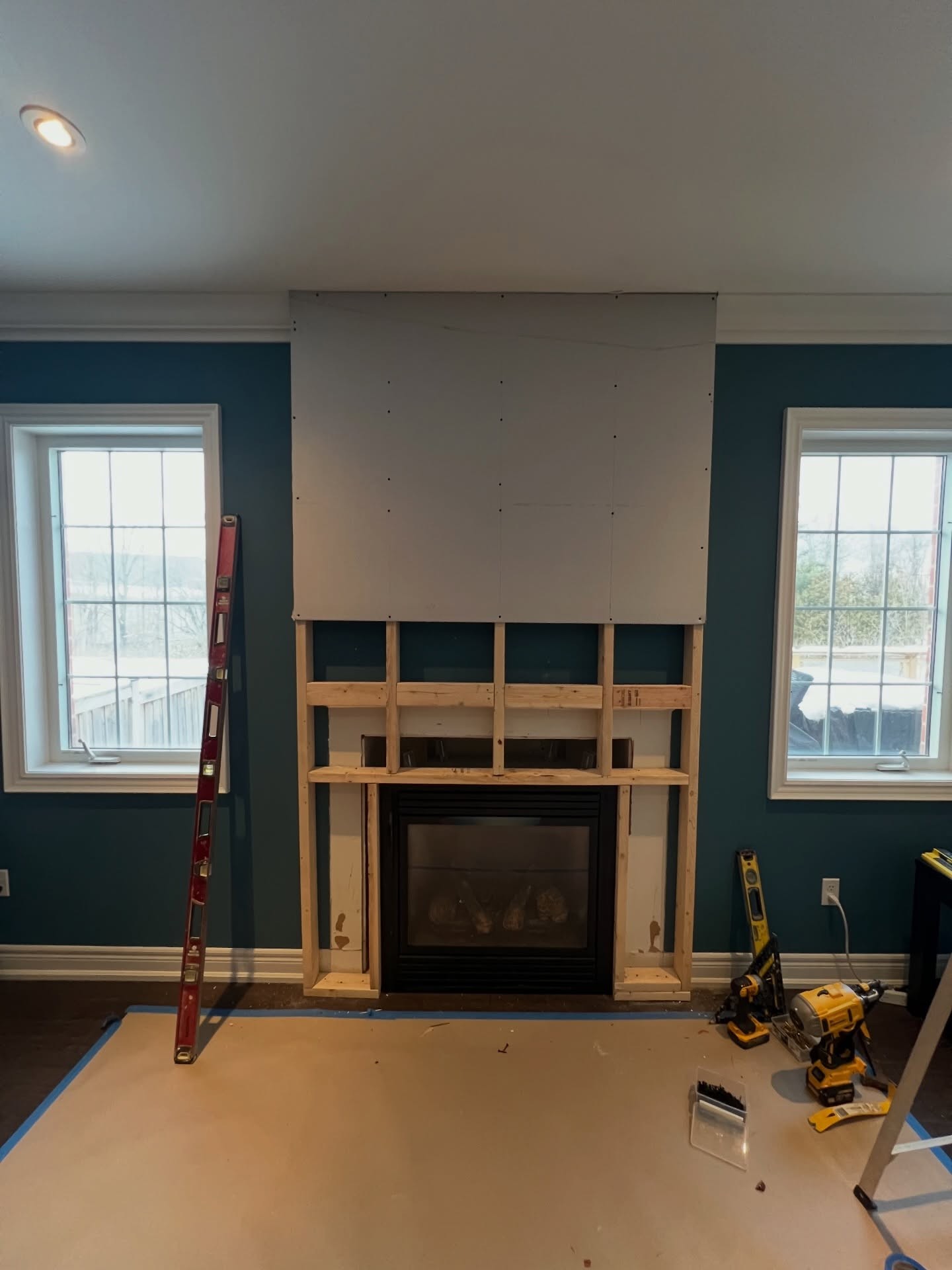 Upper half of the fireplace wall covered in fresh drywall sheets while the lower section still shows the framed opening around the original black gas insert.