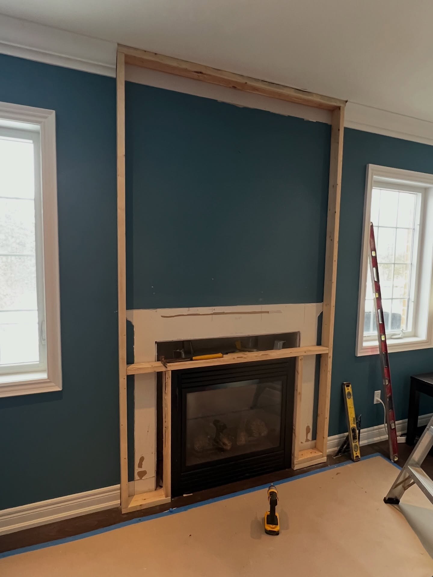 Early stage of the build showing fresh 2x4 lumber framing a tall rectangle from floor to ceiling around the existing fireplace, with the old dark mantel partly dismantled.