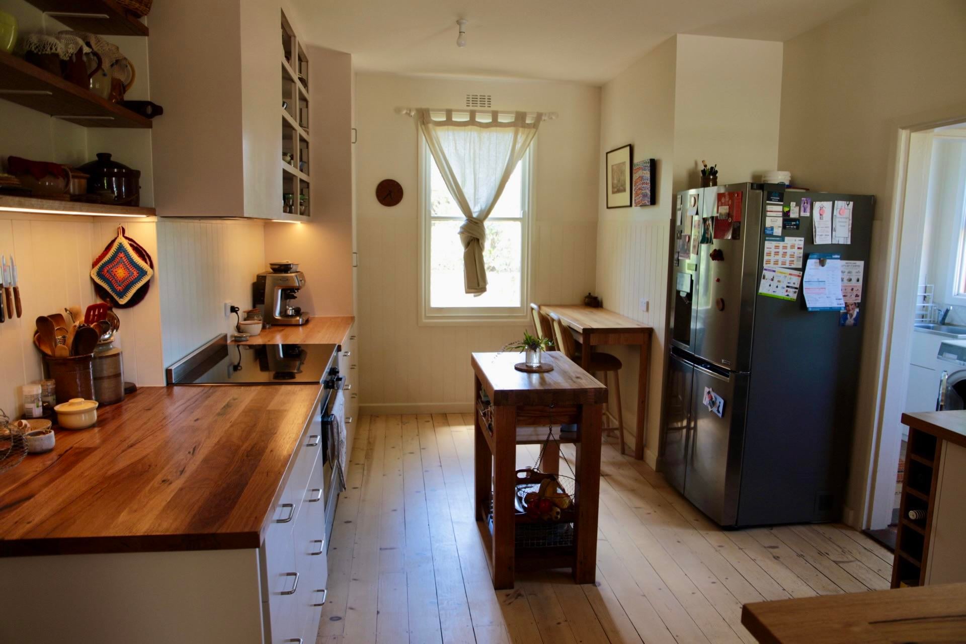 Finished kitchen with hardwood countertops, white cabinets, a wood butcher block island, a stainless fridge, pale pine floors, and a curtained window.