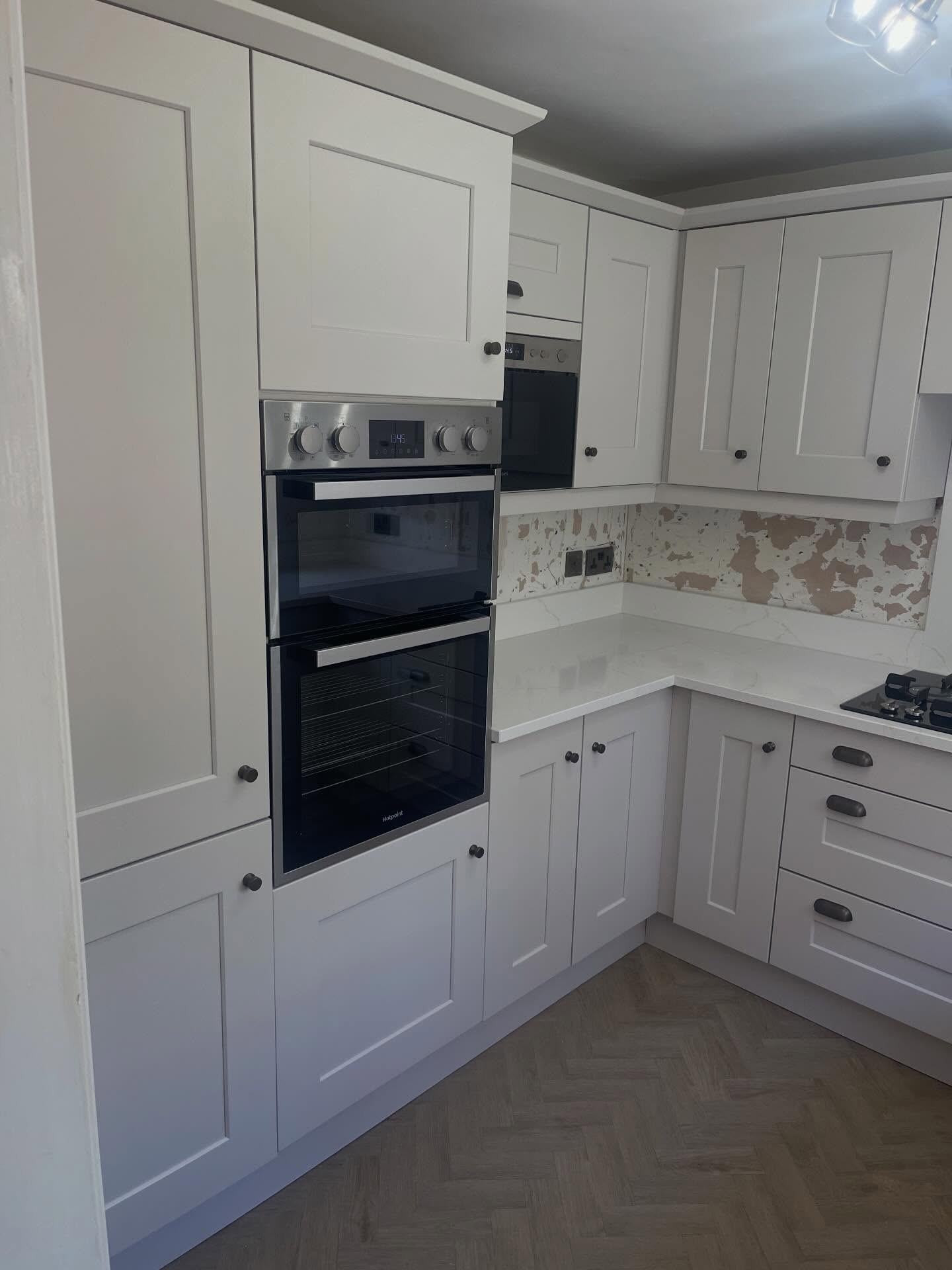 Painted Gentle Fawn tall cabinet run with built in double ovens, burnt steel knobs and herringbone floor, part of the completed kitchen respray.