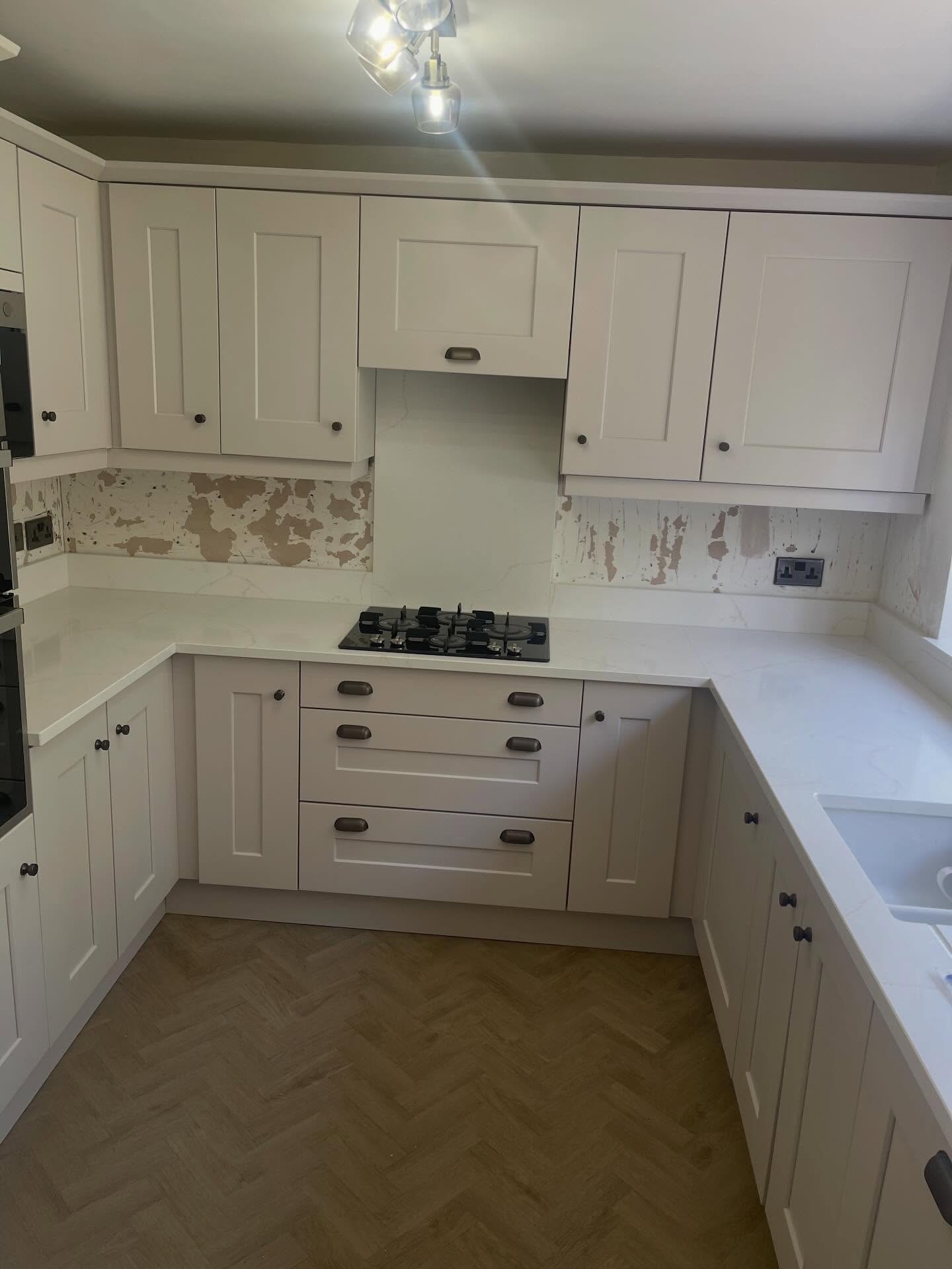 Finished Gentle Fawn kitchen in daylight showing deep drawers with burnt steel cup handles, matte quartz counter, gas hob and herringbone floor, with a pale fawn upper cabinet run matching the lower run.