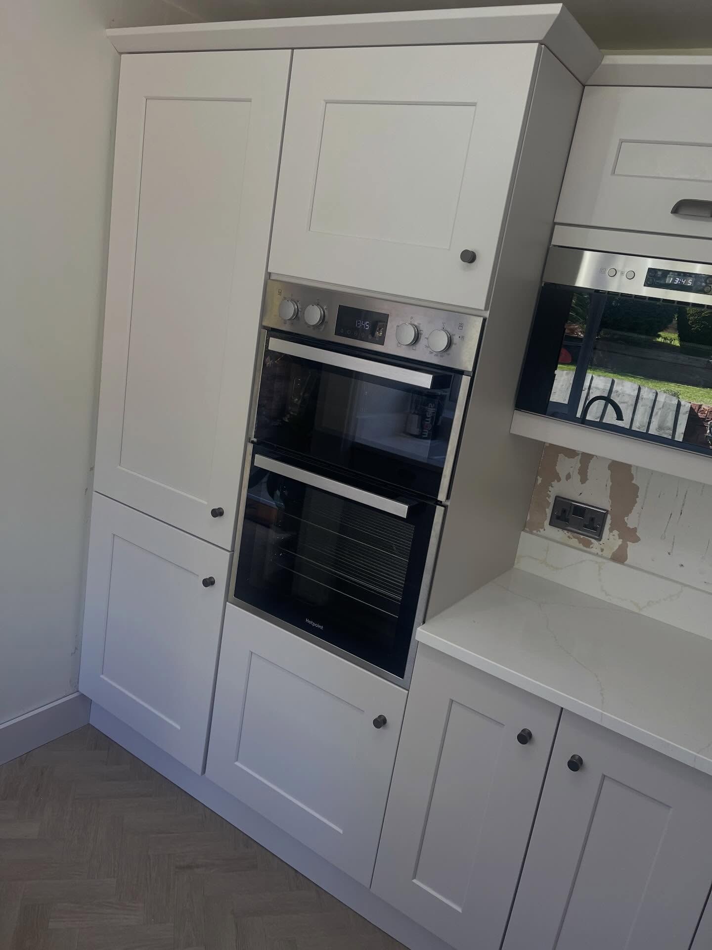 Wider view of the finished Gentle Fawn oven stack showing full height cabinets flanking the double oven, soft matte paint and warm quartz corner to the right.