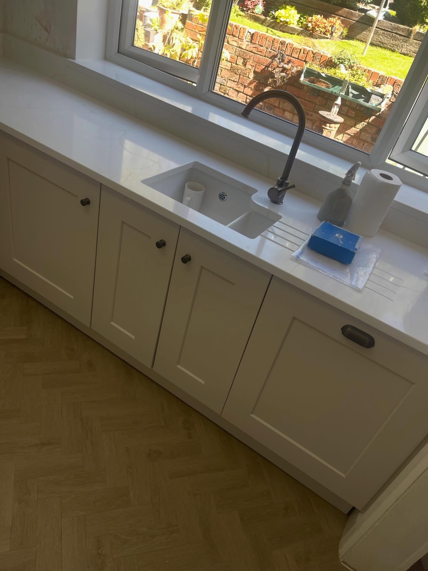 Close up of the finished quartz drainer and undermount sink with matte black gooseneck tap, Gentle Fawn cabinets below and the garden visible through the window.