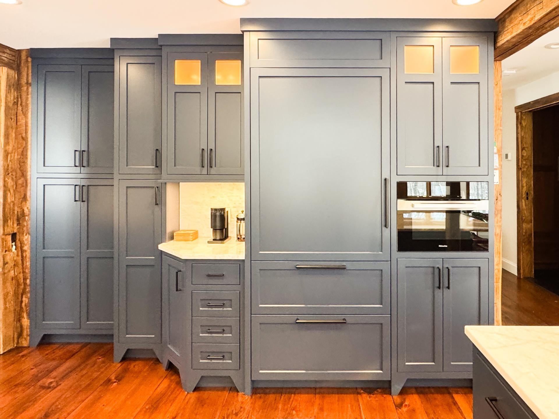 Full wall of navy cabinets with a built-in coffee station, a panel-ready fridge, a Miele wall oven, and glass-front upper cabinets with warm interior lights.