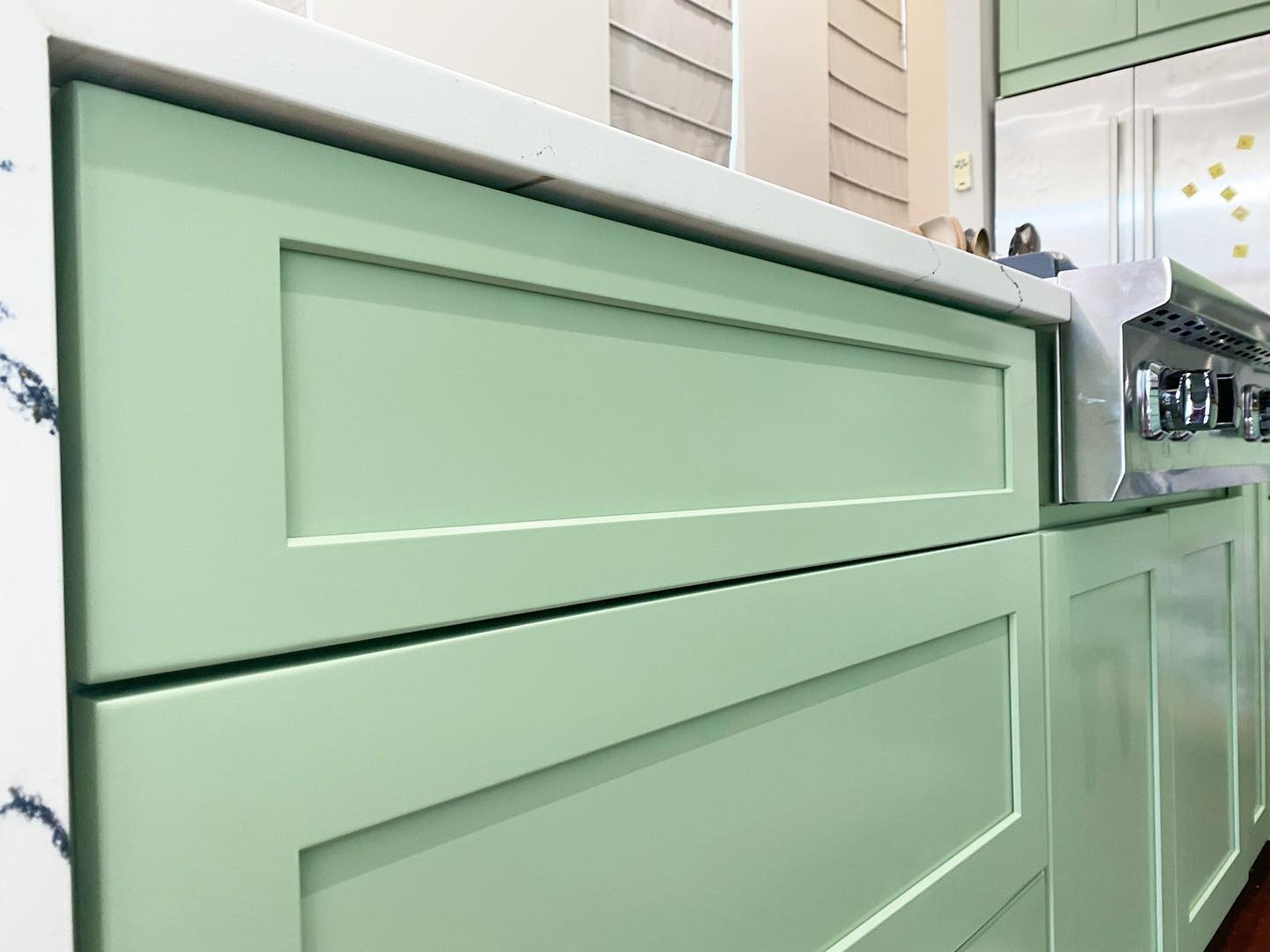 Close-up of a Haven green cabinet drawer front showing the smooth sprayed finish, shaker frame profile, and Cambria quartz countertop edge above.