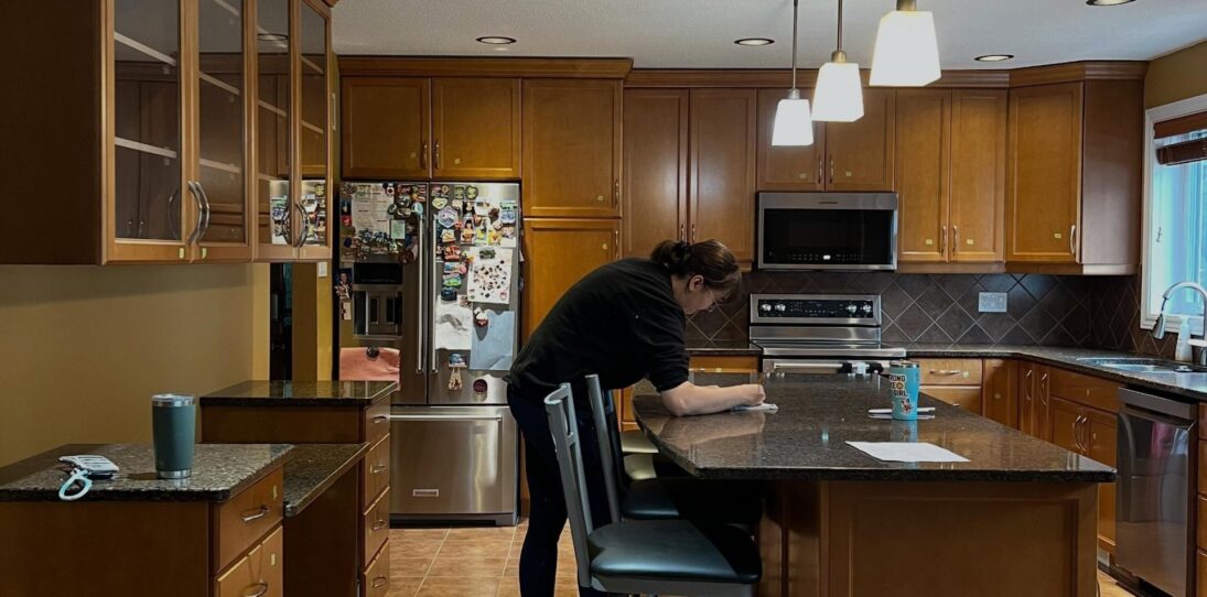 Wide view of a honey oak kitchen before painting, with orange-stained raised-panel cabinets, dark speckled brown granite counters, brown diamond-pattern tile backsplash, warm terracotta tile floor and stainless steel appliances.