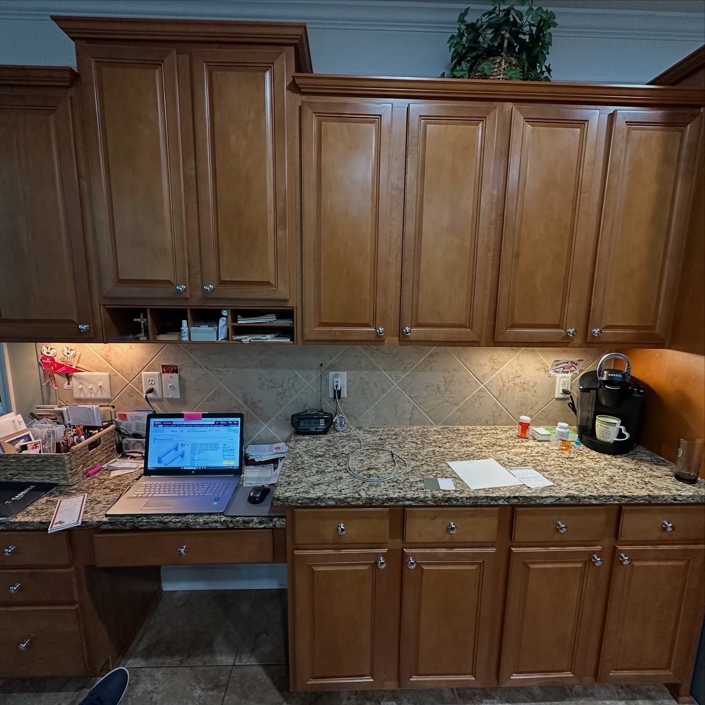 Built-in desk area with orange oak cabinets and drawers, a laptop on the counter, a Keurig coffee machine, the same cream and brown granite, and the same diamond-set tile backsplash.