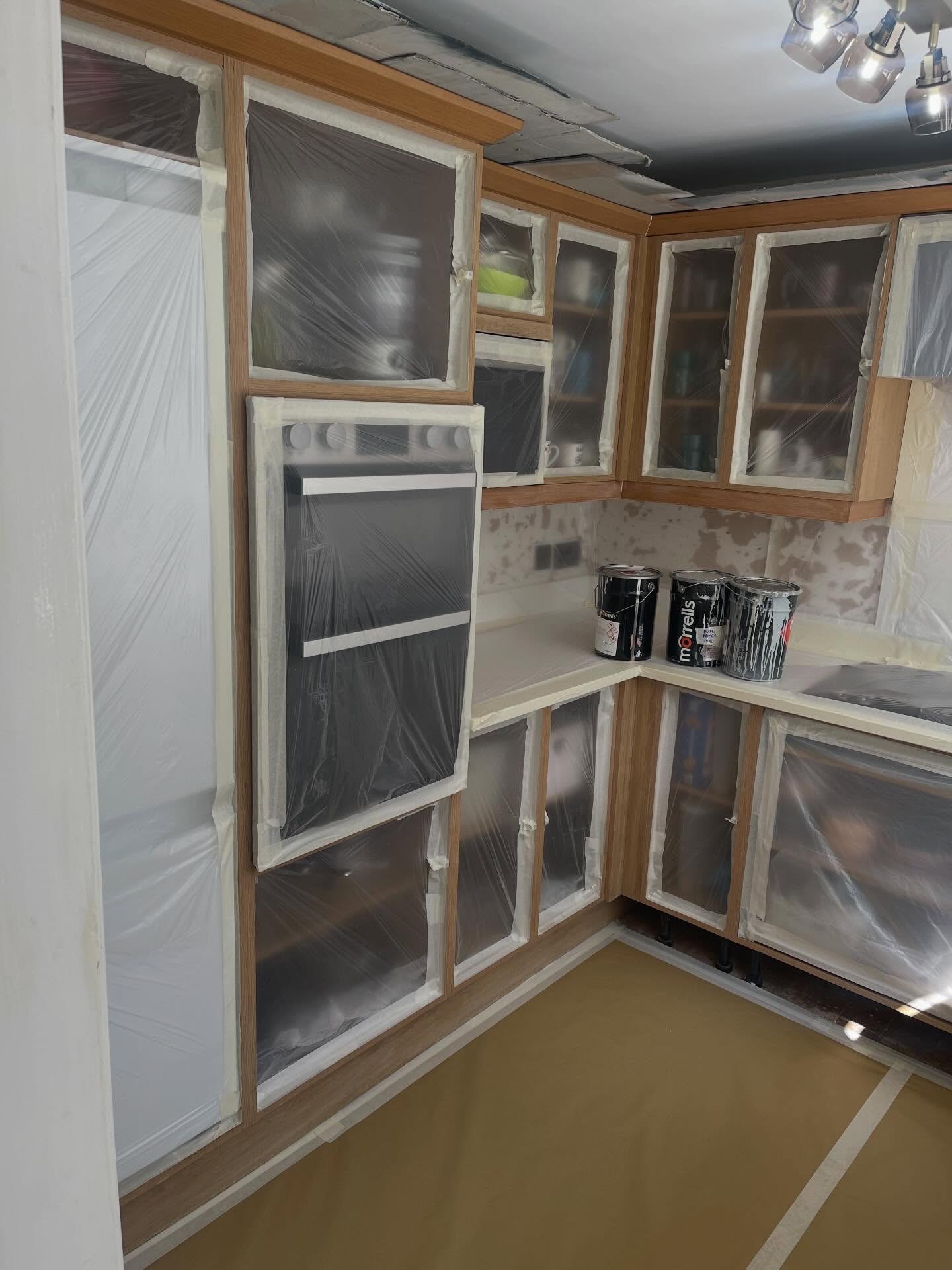 Oak kitchen with every single cabinet, oven, hob and worktop sealed under plastic sheeting and tape, floor covered in brown paper, ready for primer and top coat.