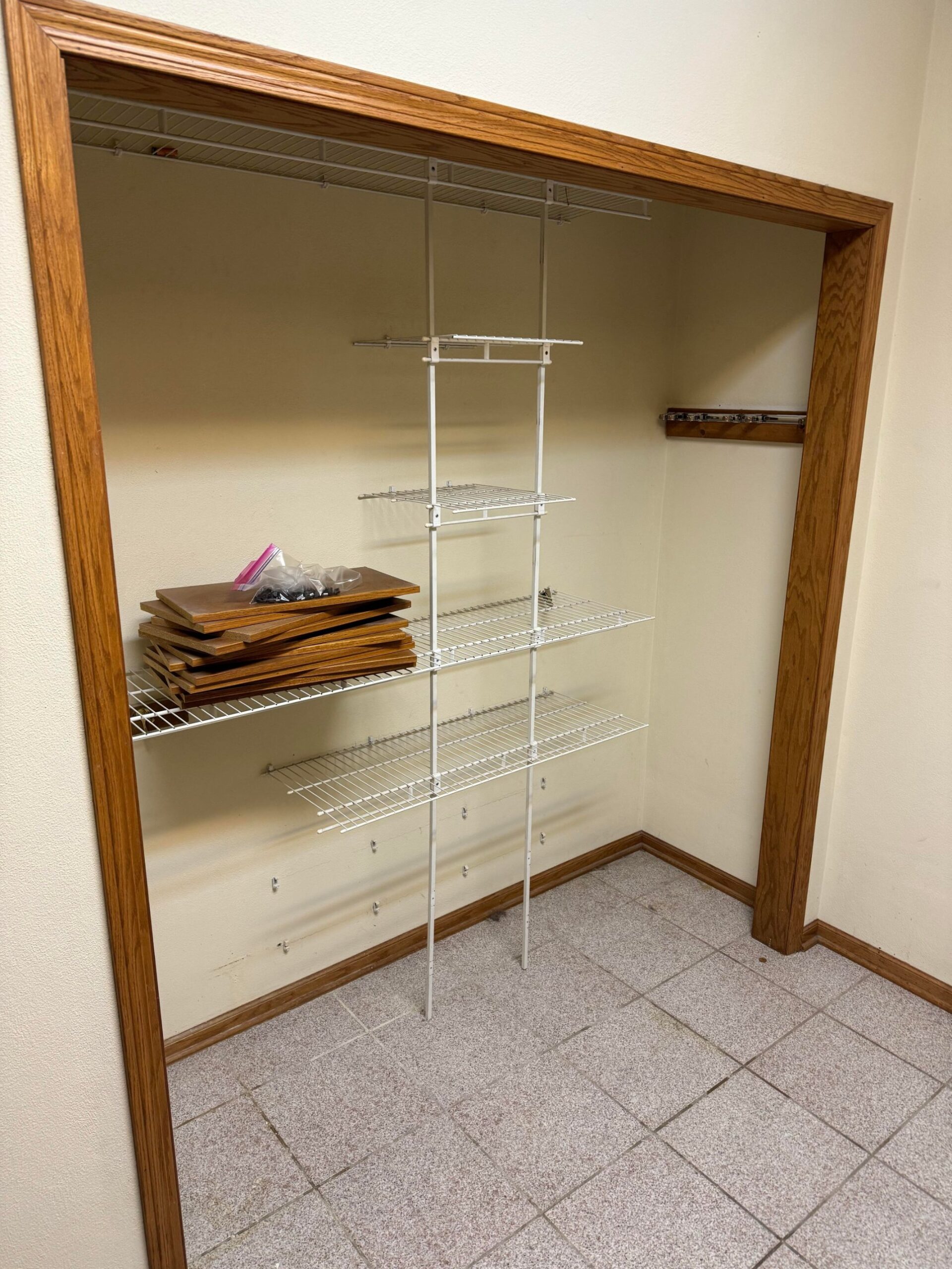 Walk-in laundry closet with white wire shelving mounted inside, oak door trim, and a small pile of wood cabinet doors stacked on one shelf, otherwise completely empty.