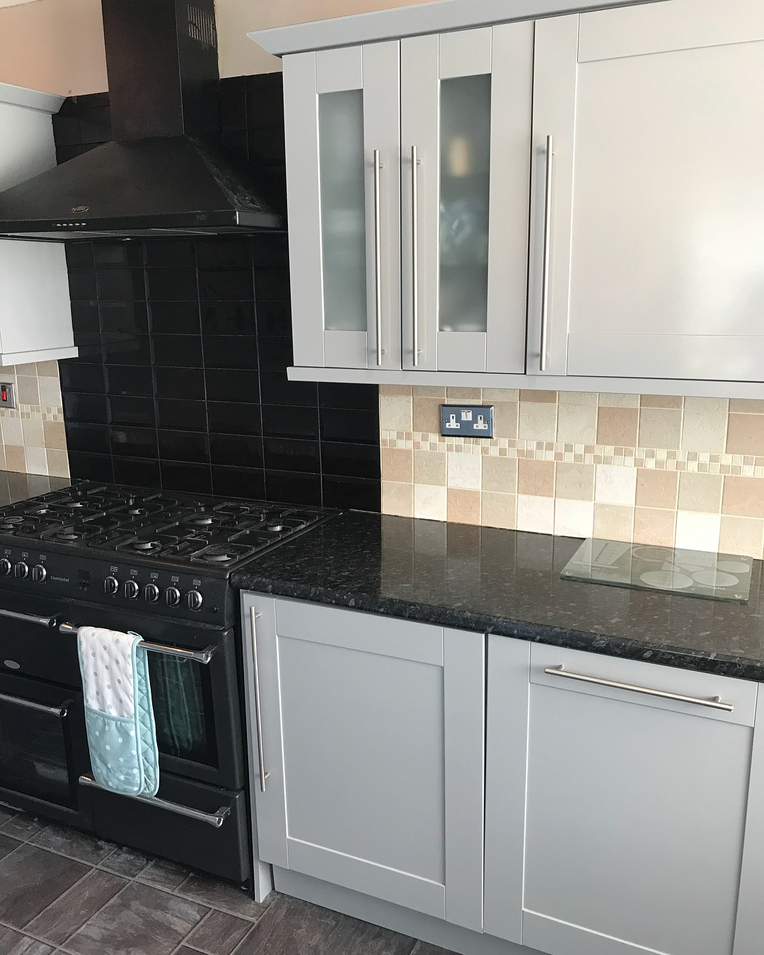 Close view of the painted gray cabinets beside the black range cooker and black tile backsplash, with the gloss finish catching the light along the Shaker panel edges.