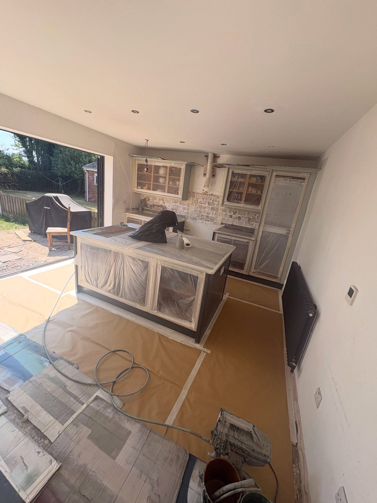 Kitchen fully masked with plastic sheeting and brown paper, cabinets taped off, floor covered, ready for the respray.
