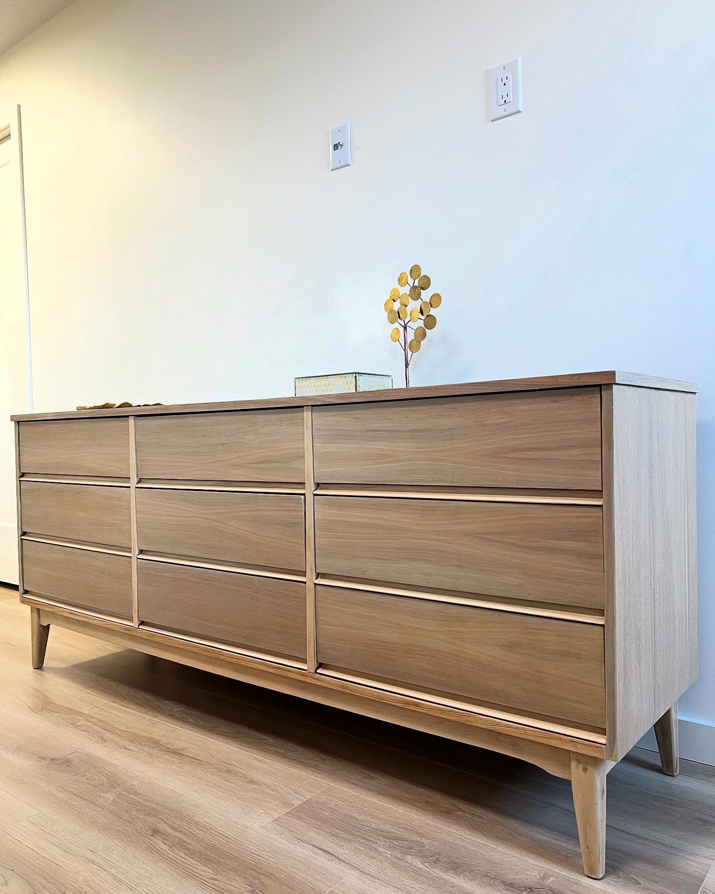 Full front view of the refinished mid-century modern tall chest in warm honey walnut, five drawers stacked on tapered legs, two glass candlesticks on top in a bright room.