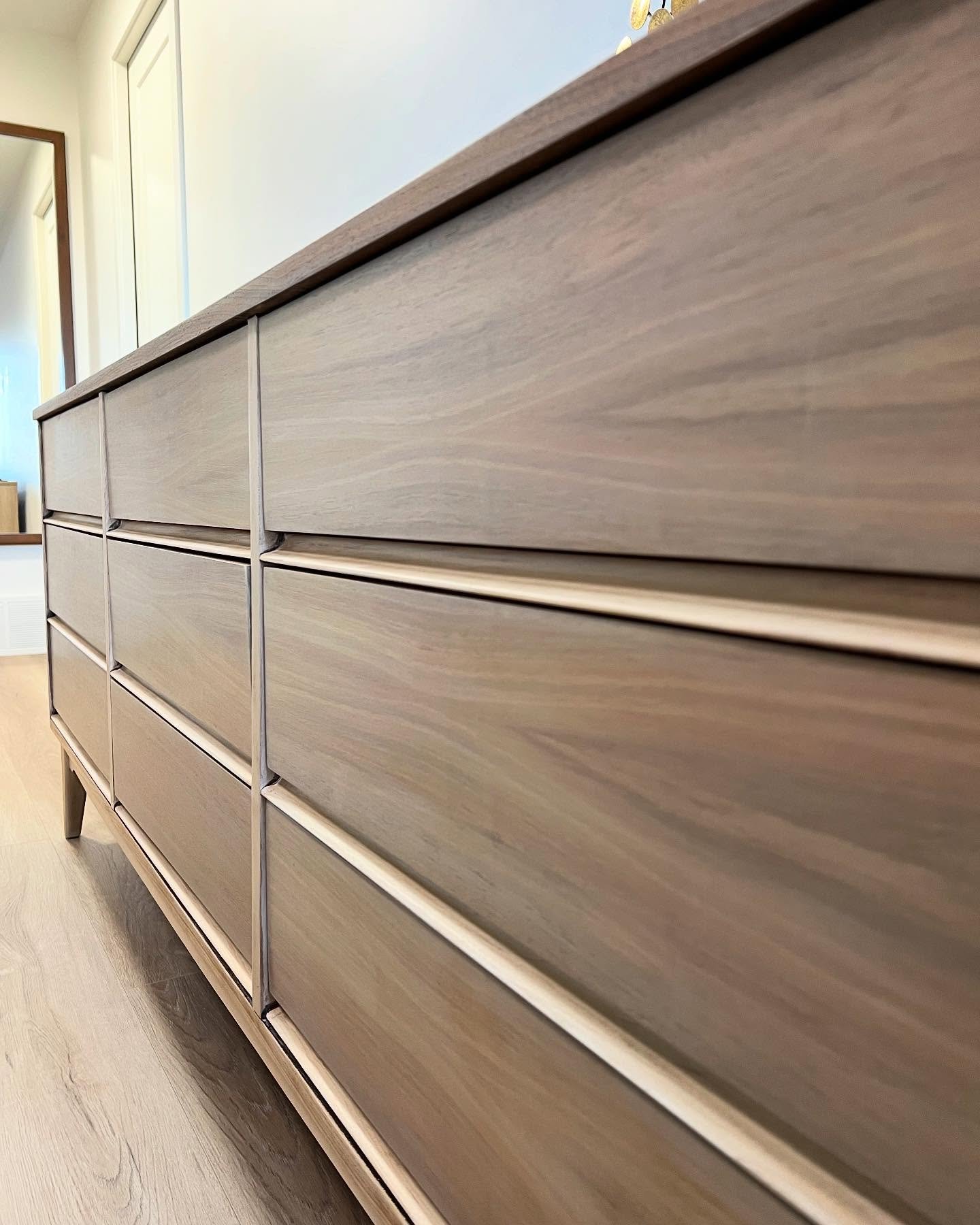 Close-up angled view of refinished mid-century modern dresser drawers showing flowing natural wood grain in a warm walnut tone, with raised wooden pulls catching light across each drawer.