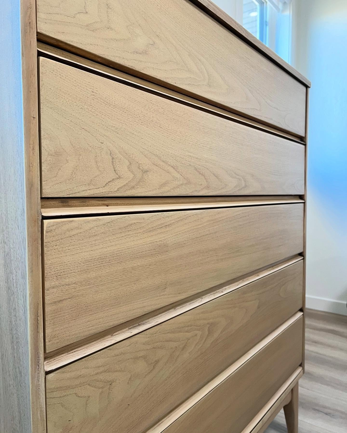 Angled view of the refinished mid-century modern tall chest in warm daylight, showing lightened walnut and the natural grain variation across all five drawers.
