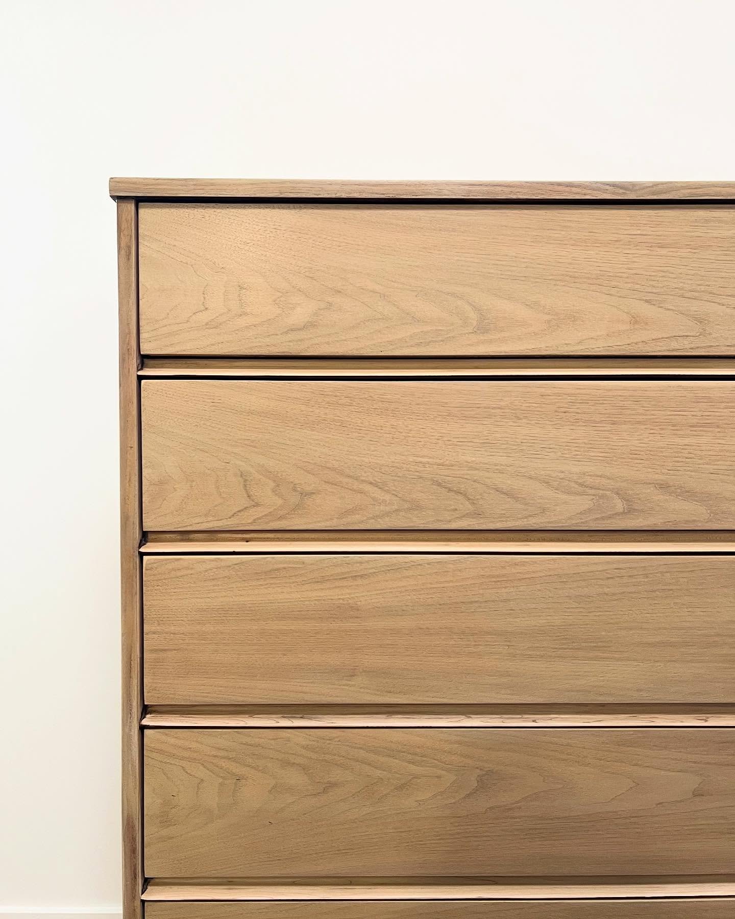 Close-up of refinished mid-century modern tall chest drawers in a soft honey walnut tone, showing dramatic chevron grain patterns running across each drawer face.