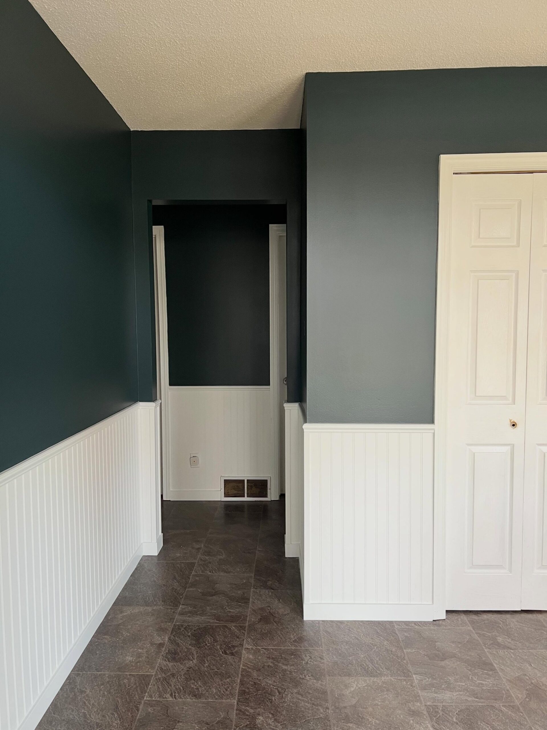 The same corner now painted deep Narragansett Green on the upper walls, white beadboard wainscoting below, dark tile floor, with the doorway opening leading into another green-painted section beyond.