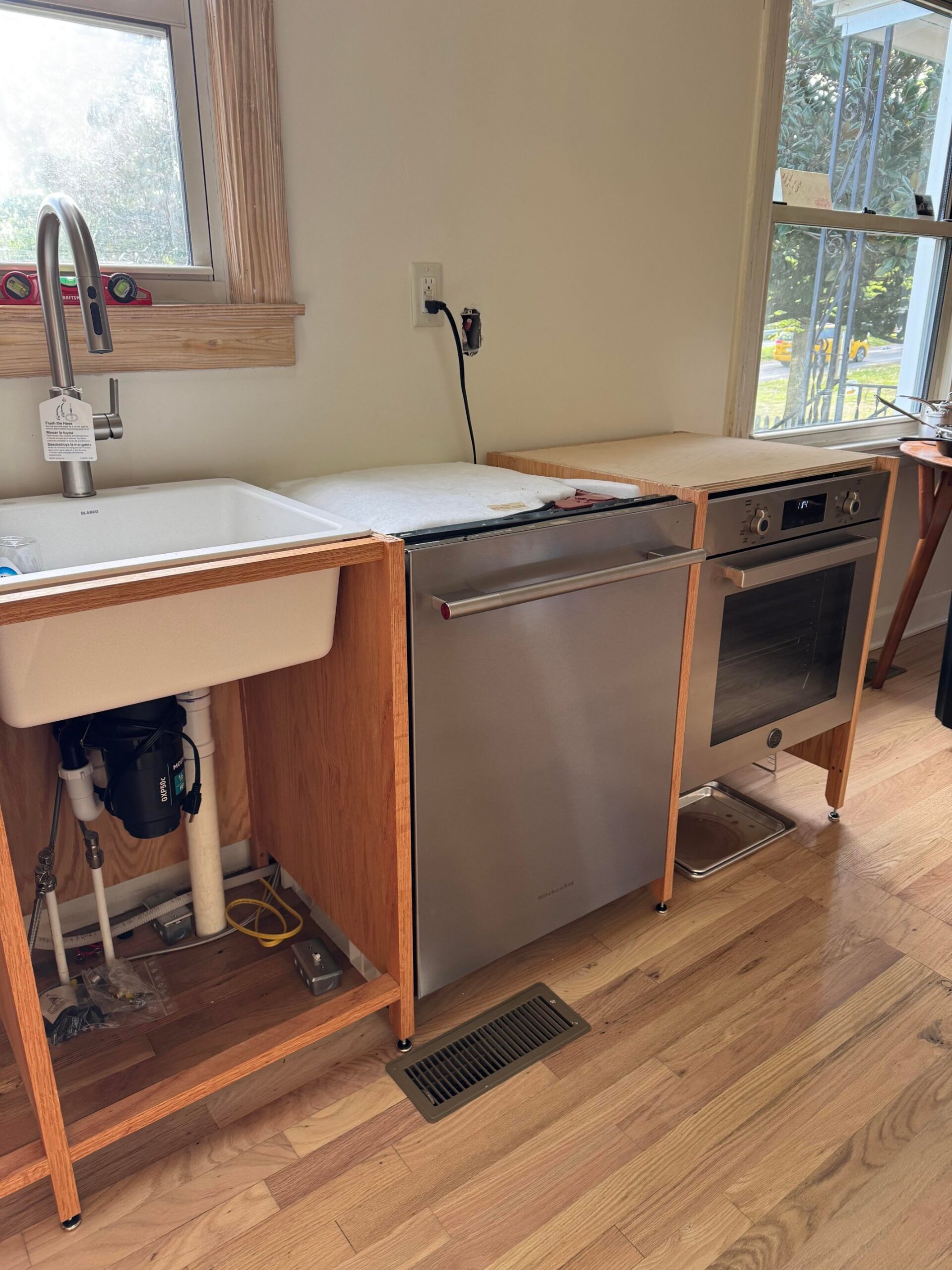 Oak cabinets with a white laundry sink and tall stainless faucet installed, cabinet fronts still missing, exposed garbage disposal visible below.