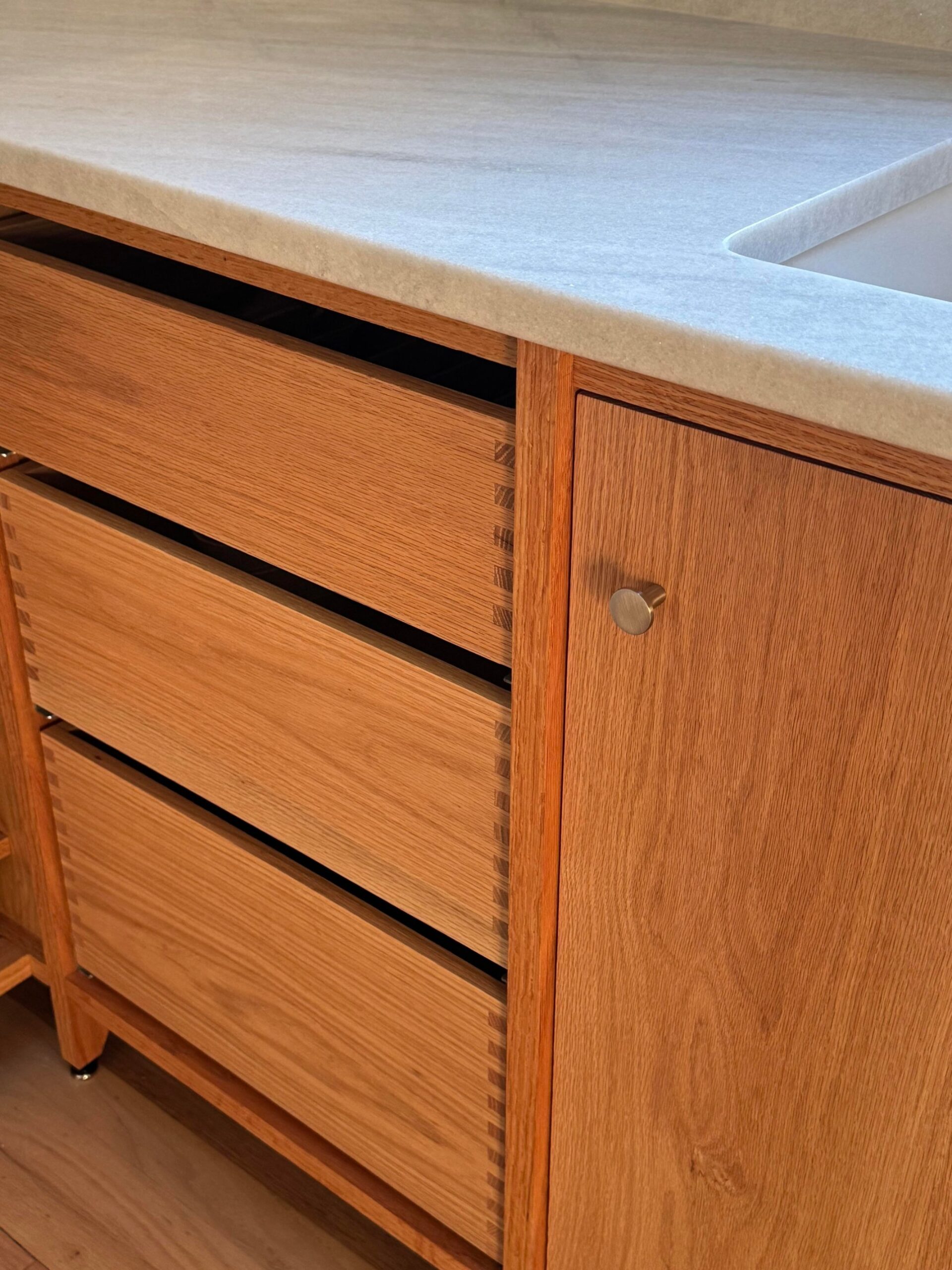 Close-up of stacked oak drawer fronts next to a solid oak door with a small brushed brass knob, box joint fingers exposed on the drawer sides.