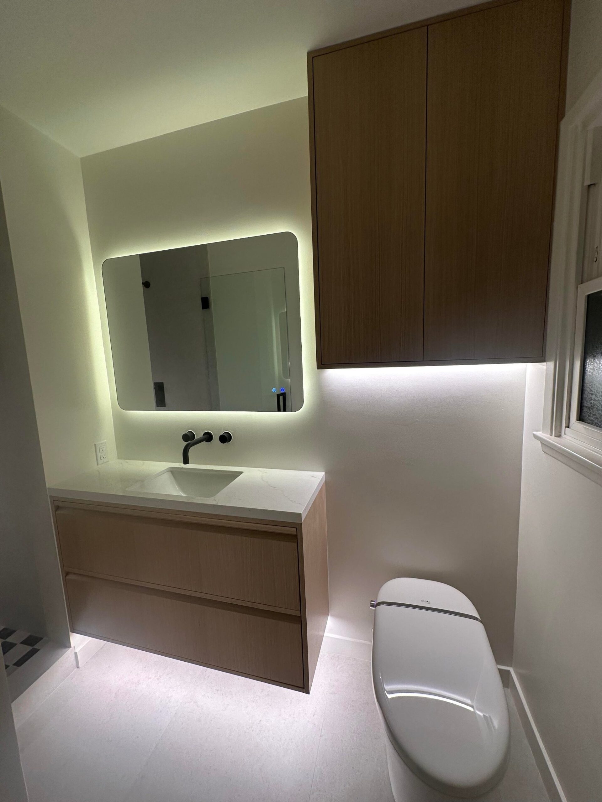 Small bathroom with orange oak cabinets, a white cultured marble vanity top, a toilet to the right, and a tall oak storage cabinet above the toilet.